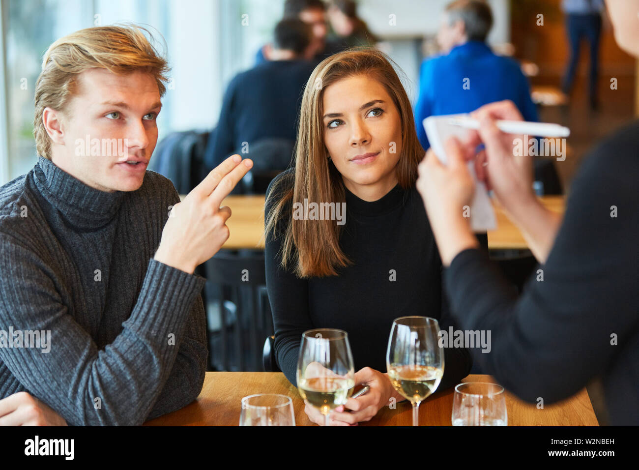 Junges Paar Bestellungen Essen beim Kellner mit Notepad im Restaurant oder Bistro Stockfoto