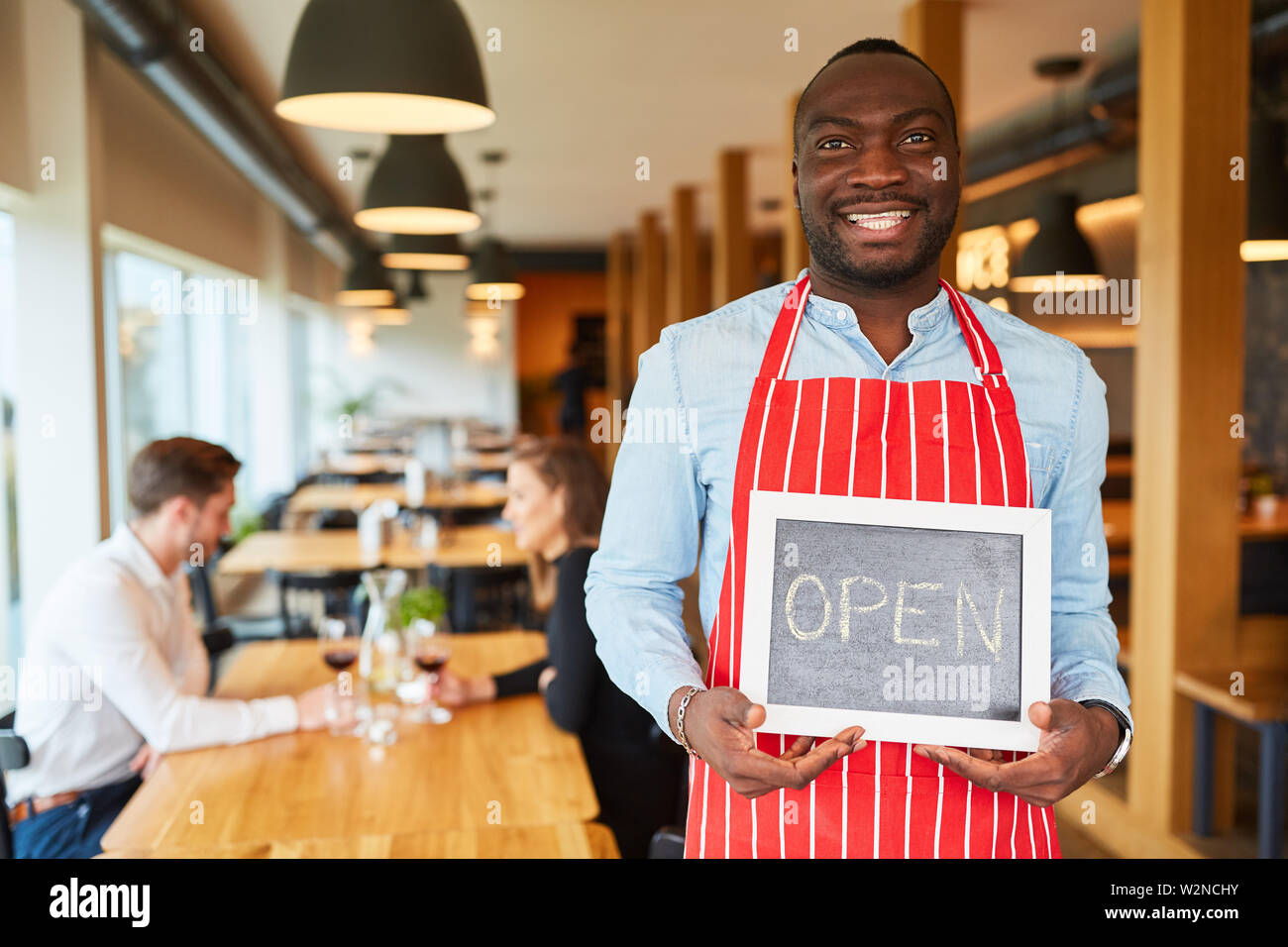 Lächelnd Kellner hält eine Tafel mit Kreide Schrift öffnen als Service Informationen Stockfoto