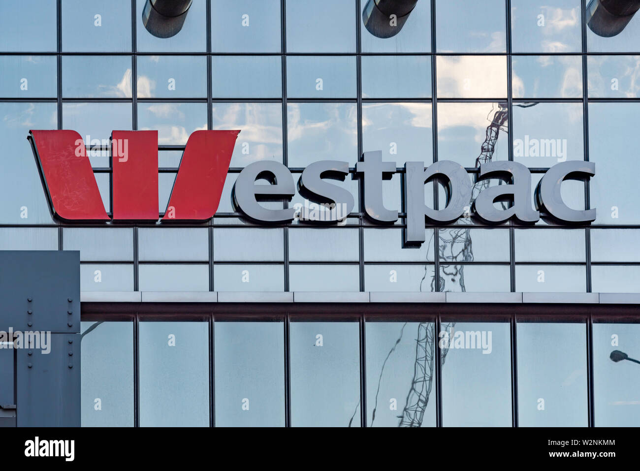 Das Logo und der Name der Australischen Westpac Bank an der Außenseite eines Gebäude aus Glas mit der Reflexion eines Krans und Wolken im Hintergrund Stockfoto