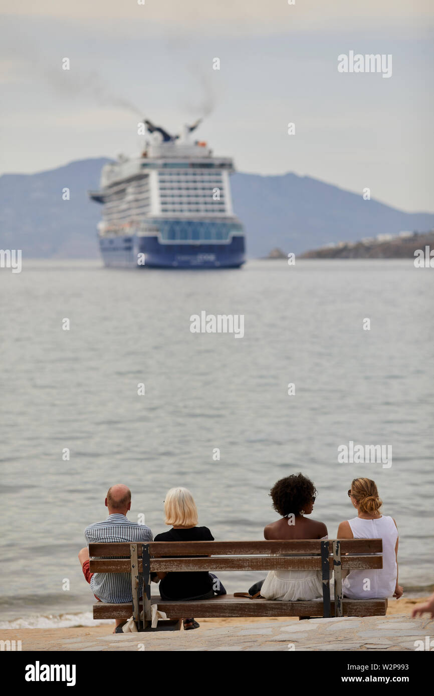 Mykonos, griechische Insel Mikonos, Teil der Kykladen, Griechenland. Touristen auf a waterfront Beach Bank auf Berühmtheit Kante zuerst Edge-Klasse Kreuzfahrt s Stockfoto