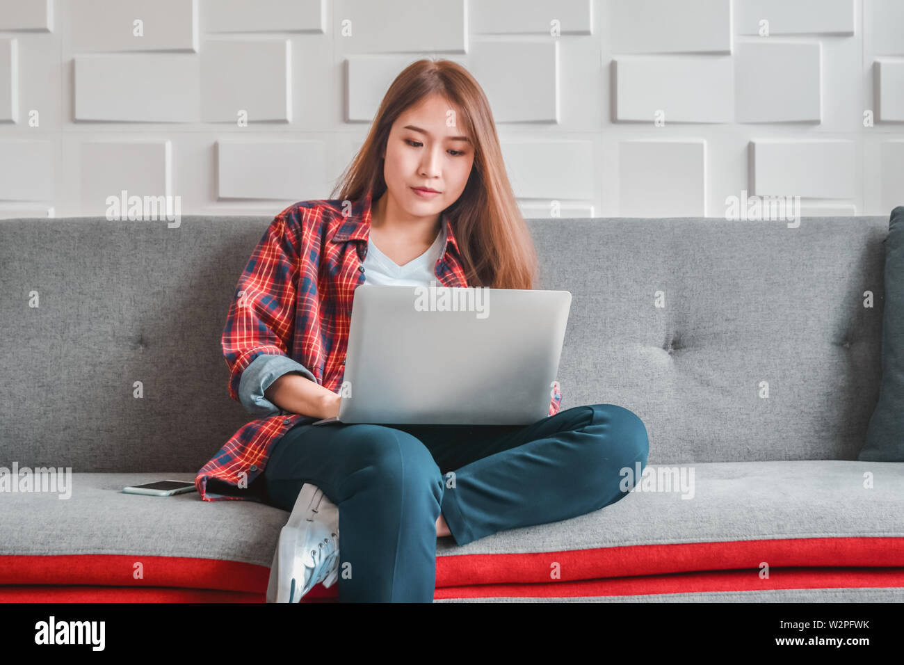 Junge Frau in Freizeitkleidung mit Laptop Computer sitzen entspanntes Arbeiten am heimischen Sofa im Wohnzimmer zufrieden und Ruhe genießen in der Technologie Stockfoto