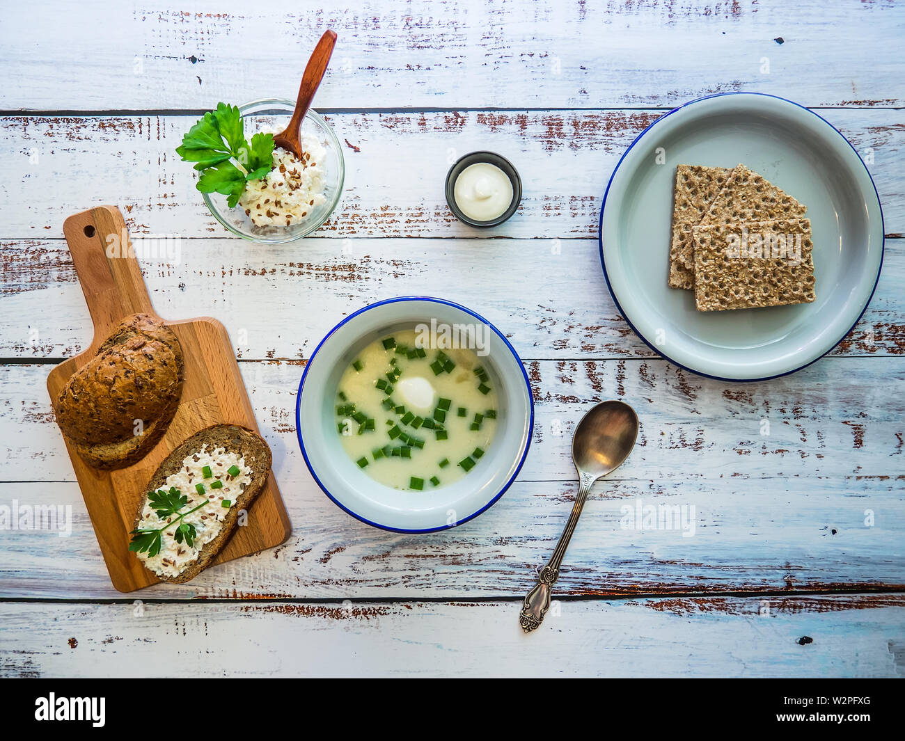 Abendessen auf einem rustikalen Holztisch: eine Schüssel mit Suppe mit grünen Zwiebeln, Vollkornbrot auf einem Schneidebrett und frische Brot auf den Teller. Stockfoto