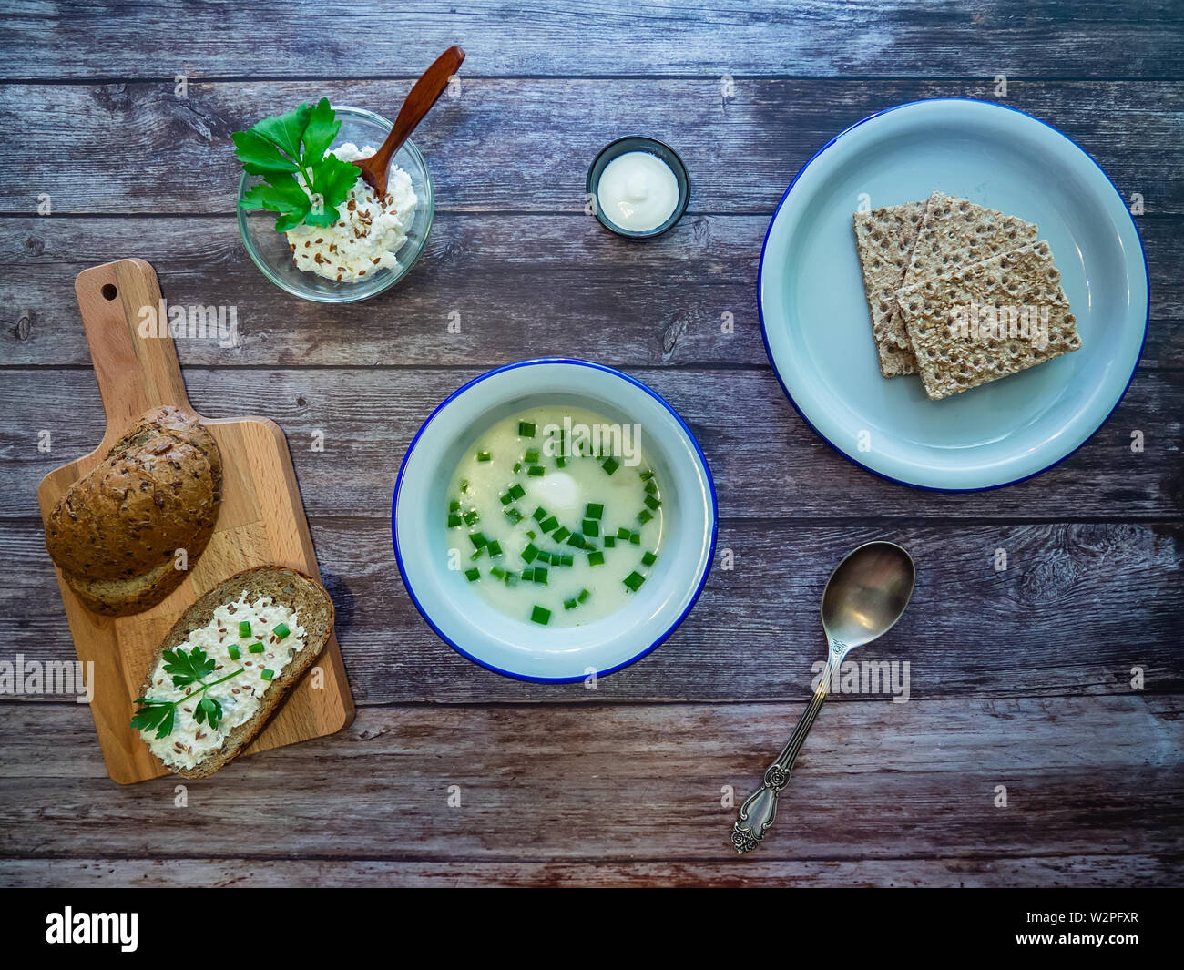 Abendessen auf einem rustikalen Holztisch: eine Schüssel mit Suppe mit grünen Zwiebeln, Vollkornbrot auf einem Schneidebrett und frische Brot auf den Teller. Stockfoto