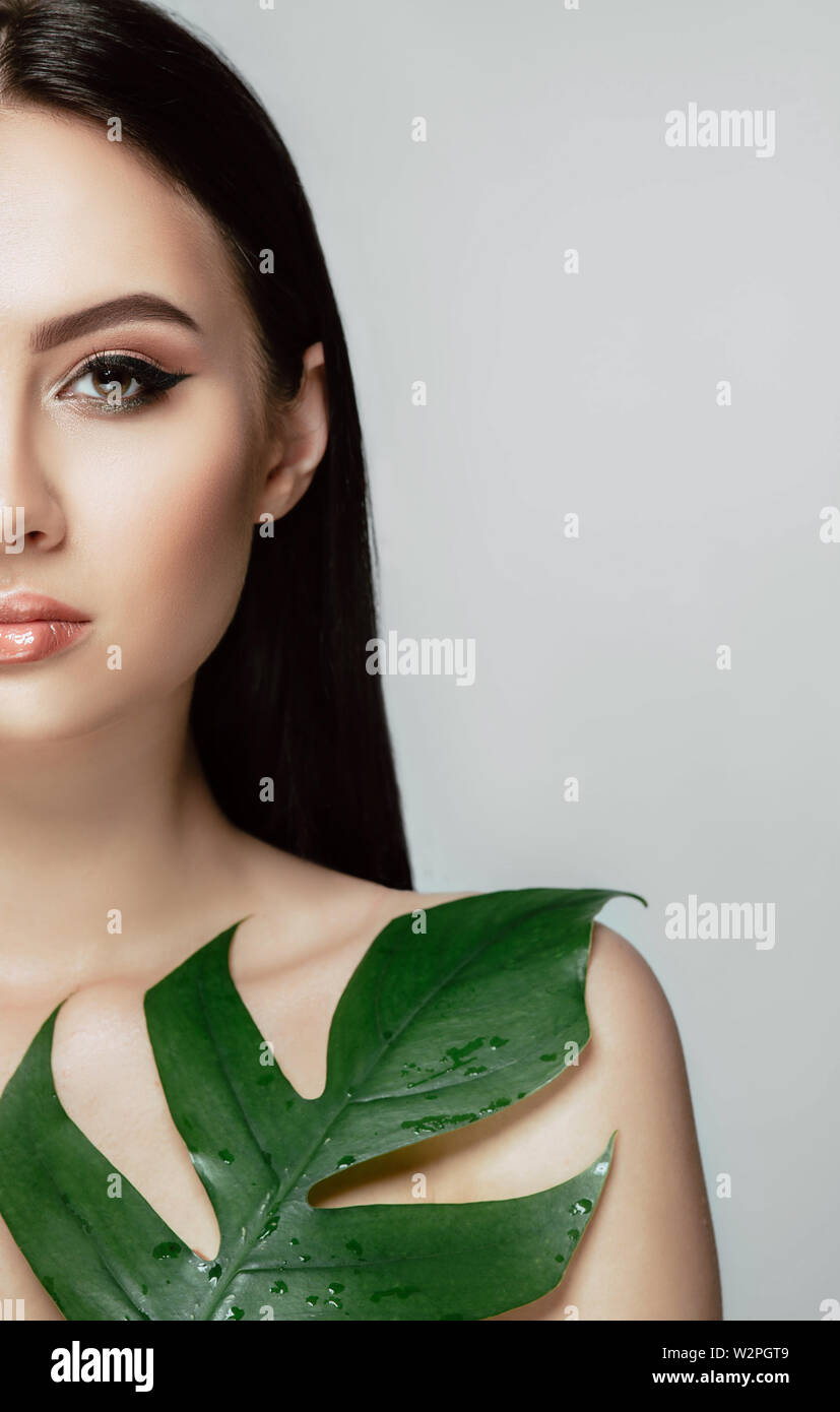 Frau mit perfektem Make-up mit Pfeil auf Auge und grünen tropischen Blatt. Natürliche organische Kosmetik Stockfoto