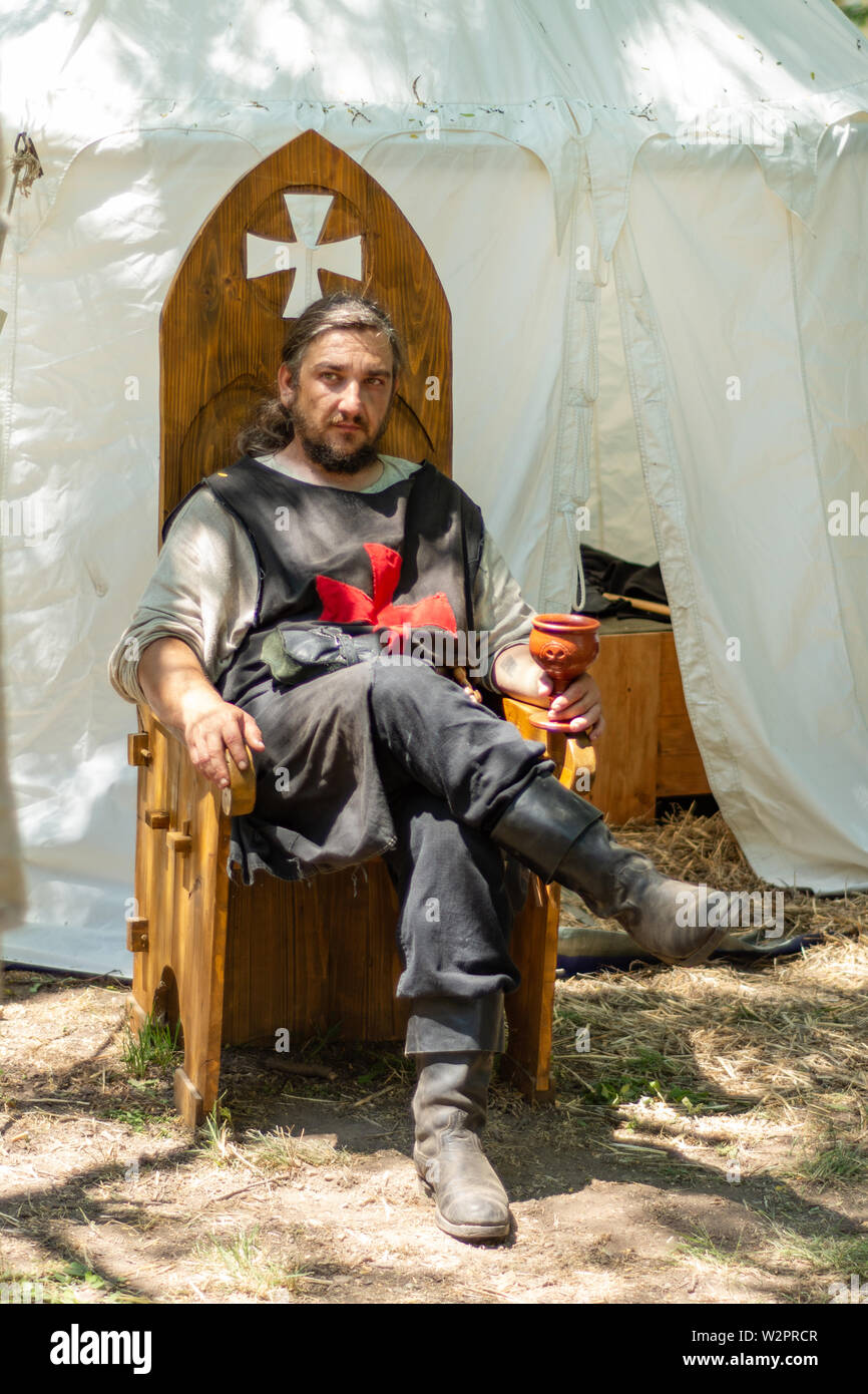 Nis, Serbien - Juni 15. 2019 Ritter in Trachten sitzt auf einem hölzernen Thron vor dem Zelt und Getränke Wein auf Ritter Festival Stockfoto