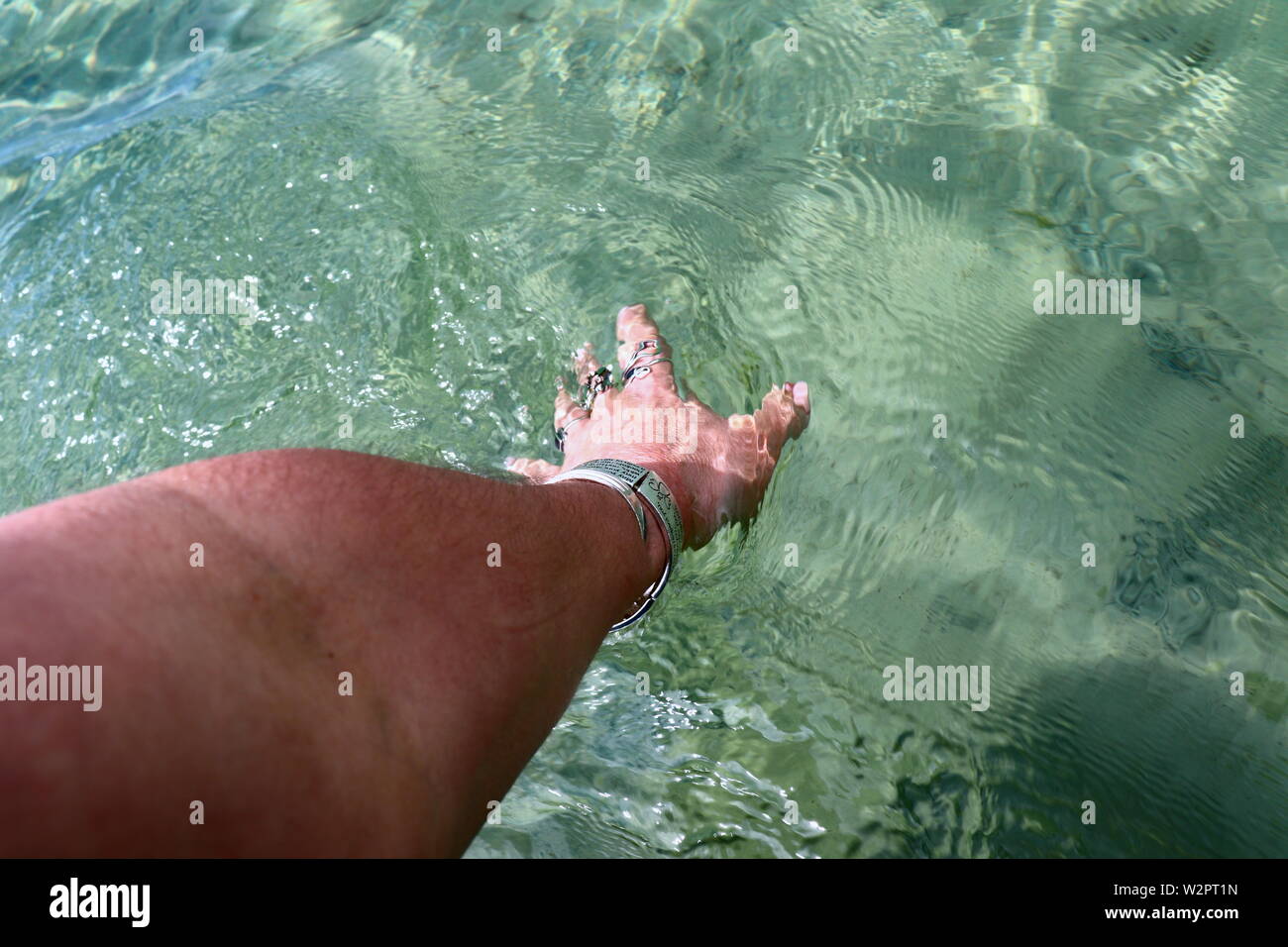 Woman's Hand mit Silber Armbänder und Ringe, Plantschen im Meer Wasser Stockfoto