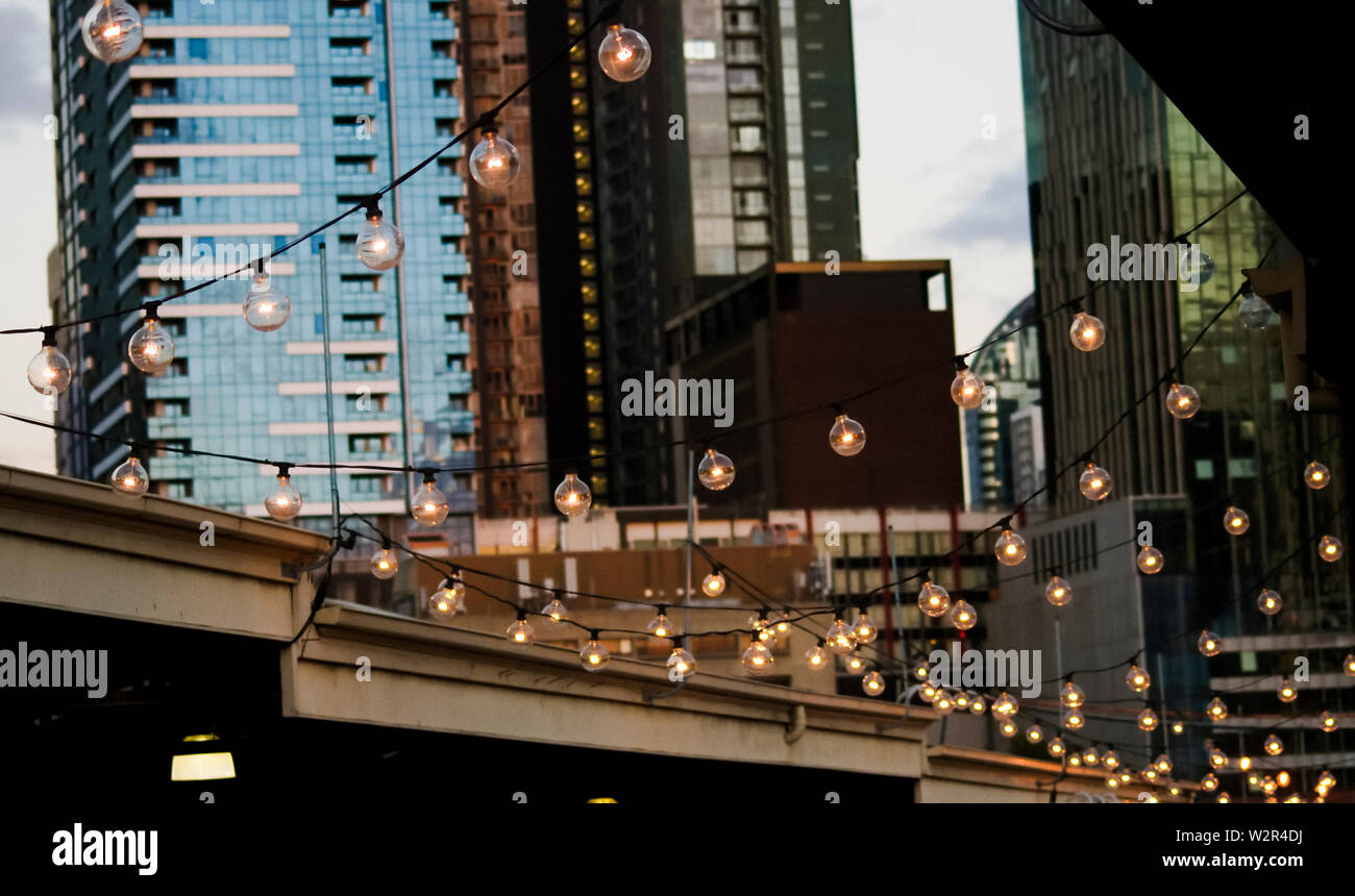 Einen hängenden Lichterkette im Queen Victoria Markets mit Blick auf die Skyline von Melbourne City im Hintergrund Stockfoto