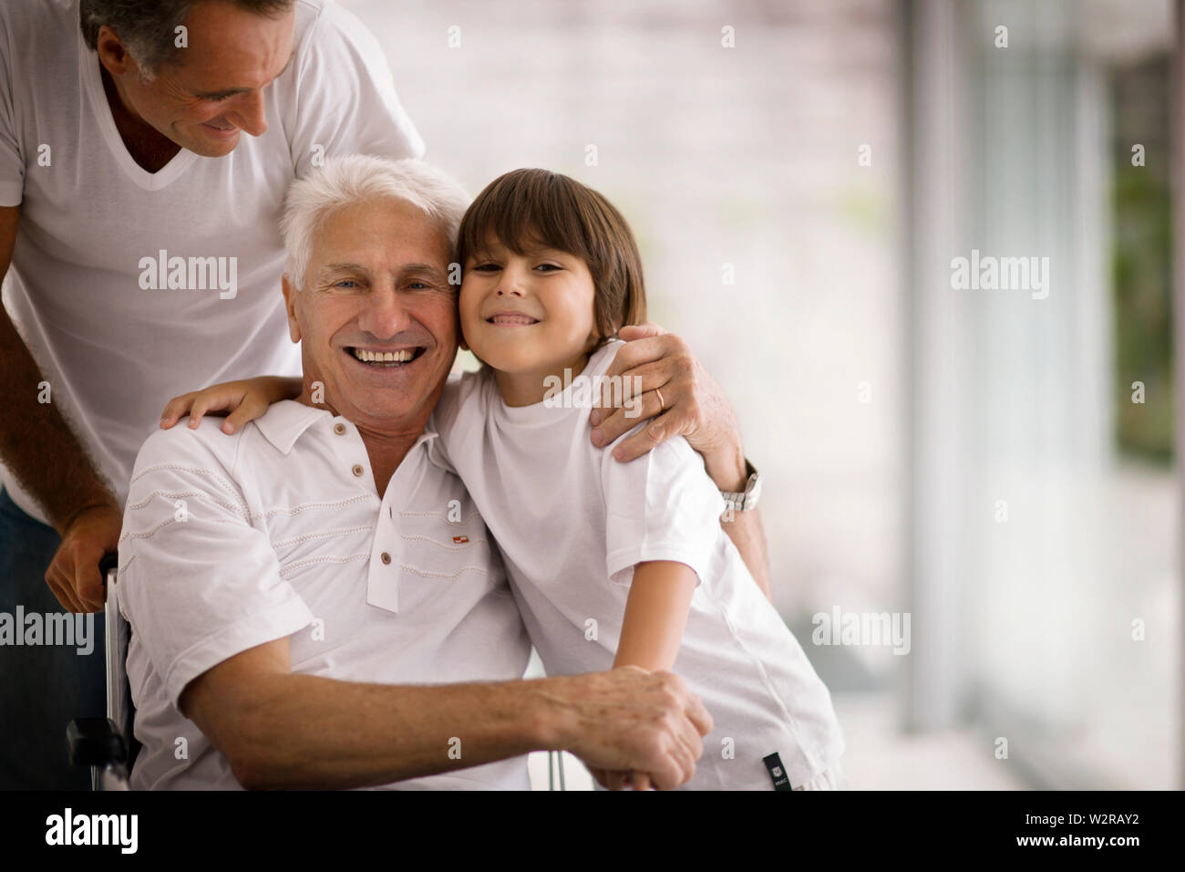 Älterer Mann im Rollstuhl umarmt seinen jungen Enkel. Stockfoto