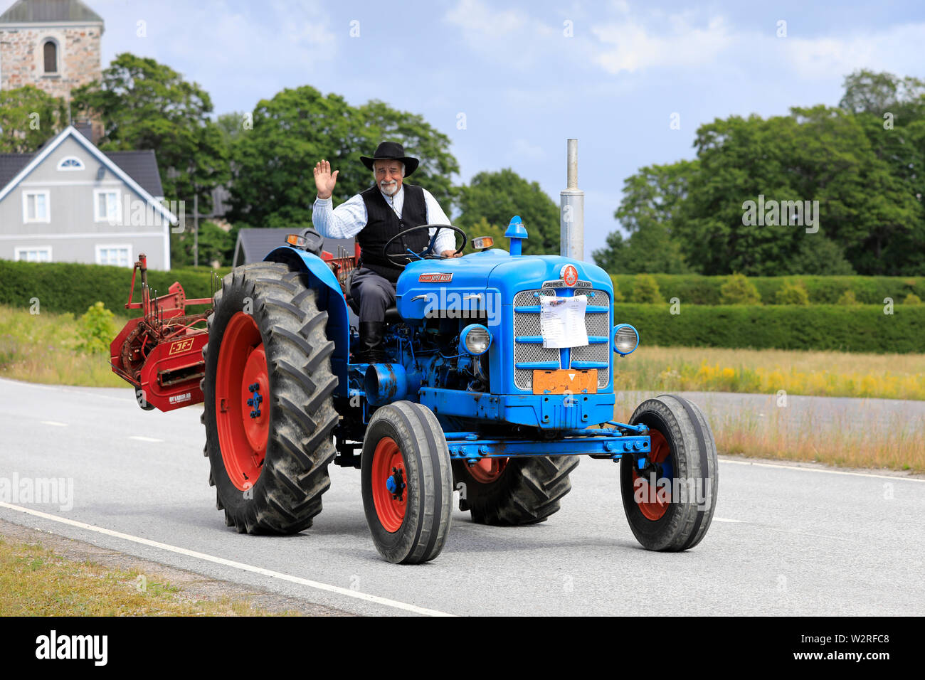 Kimito, Finnland. Juli 6, 2019. Mann in traditioneller Tracht begrüßt, als er Laufwerke Fordson Super Major auf Kimito Tractorkavalkad, vintage Traktor Parade. Stockfoto