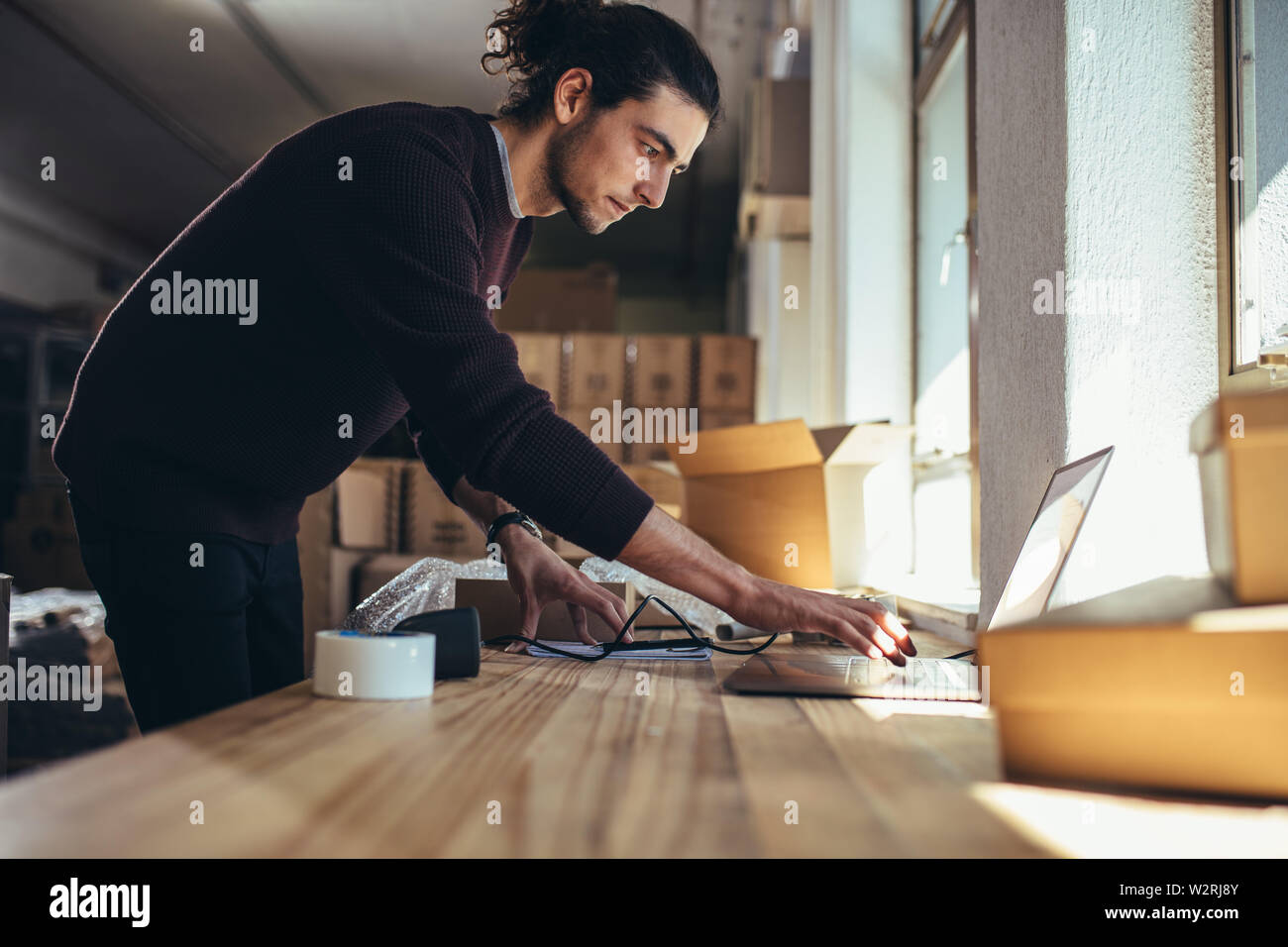 Junger Mann bei der Arbeit auf dem Laptop, nachdem die Dichtung das Paket für die Lieferung. Inhaber kleiner Unternehmen arbeiten im Büro. Stockfoto