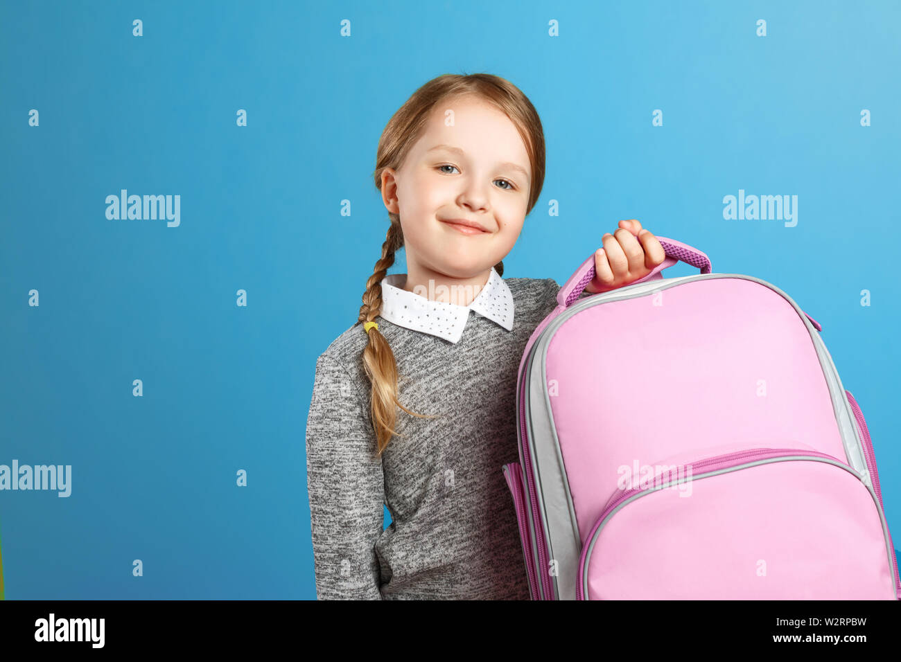 Closeup Portrait von einem kleinen Mädchen Schülerin auf einem blauen Hintergrund. Das Kind hält einen schulranzen. Zurück zu Schule. Der Begriff der Bildung. Stockfoto