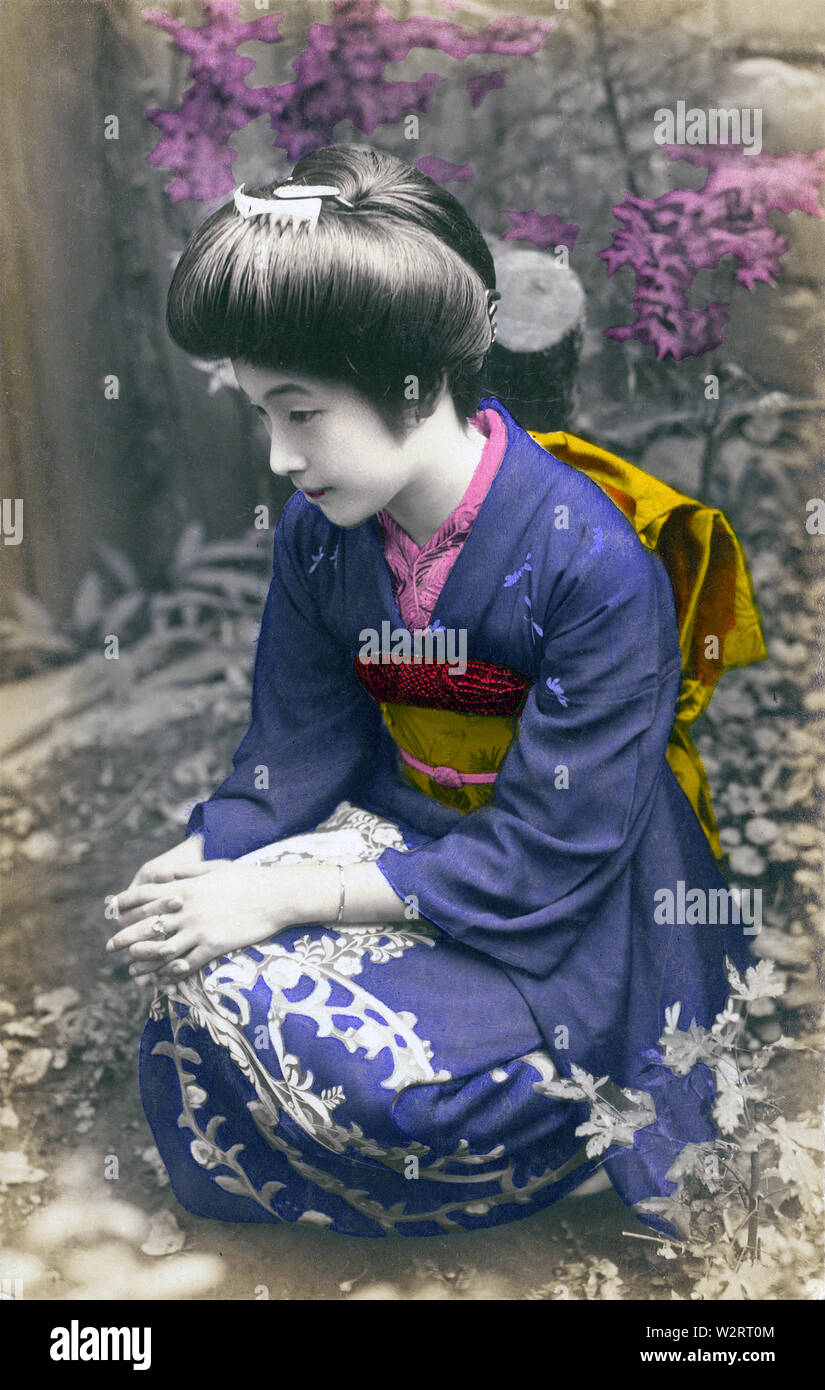 [1910s Japan - Kniend japanischen Frau im Kimono] - Frau im Kimono und traditionelle Frisur in einem Garten. 20. jahrhundert alte Ansichtskarte. Stockfoto