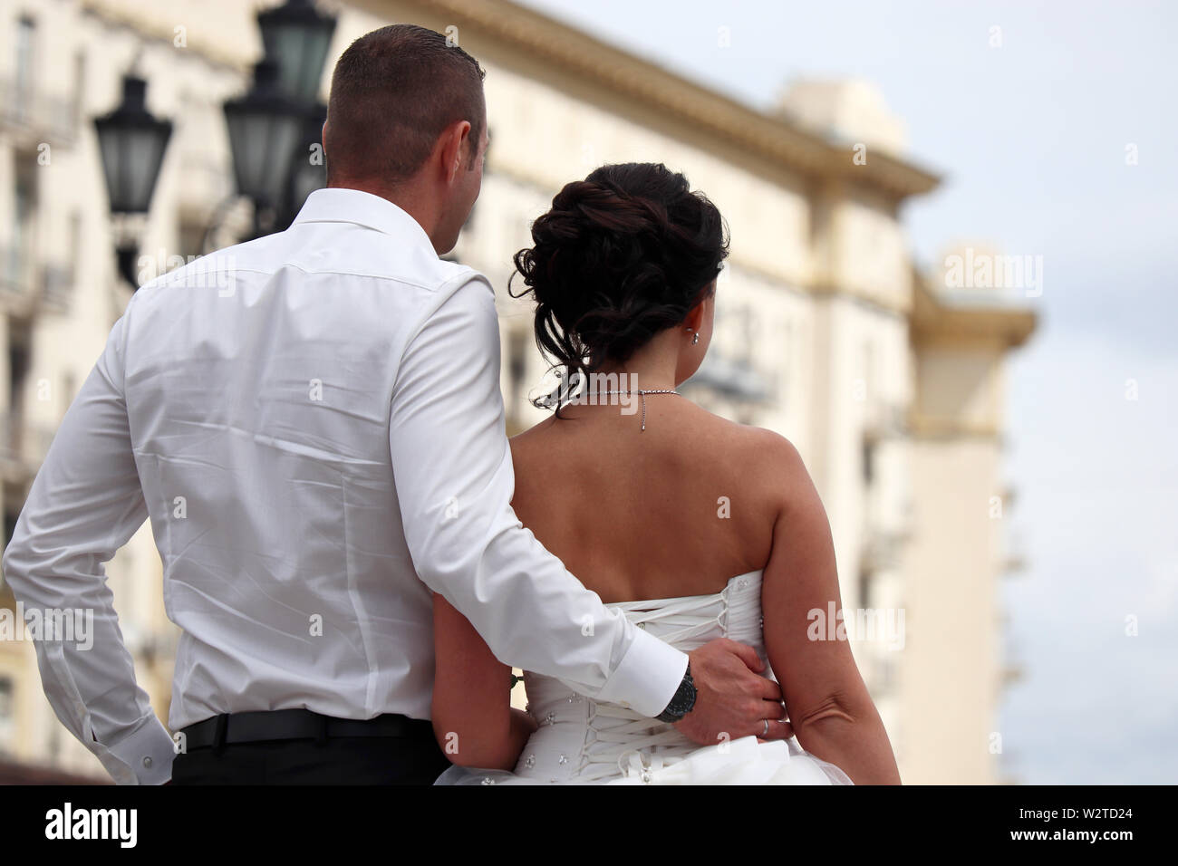 Hochzeit in einer Stadt, Bräutigam umfasst die Taille der Braut, Ansicht von hinten. Frisch verheiratete Ehepaar, das Konzept der neuen Familie mit Blick auf die Zukunft Stockfoto