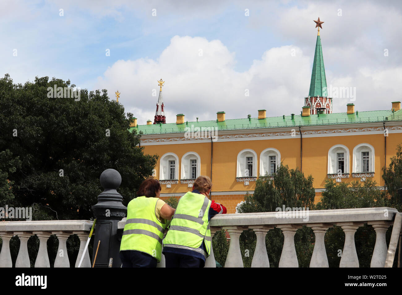 Hausmeister mit einem Besen auf Hintergrund der Moskauer Kreml, zwei Frauen in der Uniform der kommunalen Arbeitnehmer im Sommer. Migranten, Straßenreinigung Stockfoto