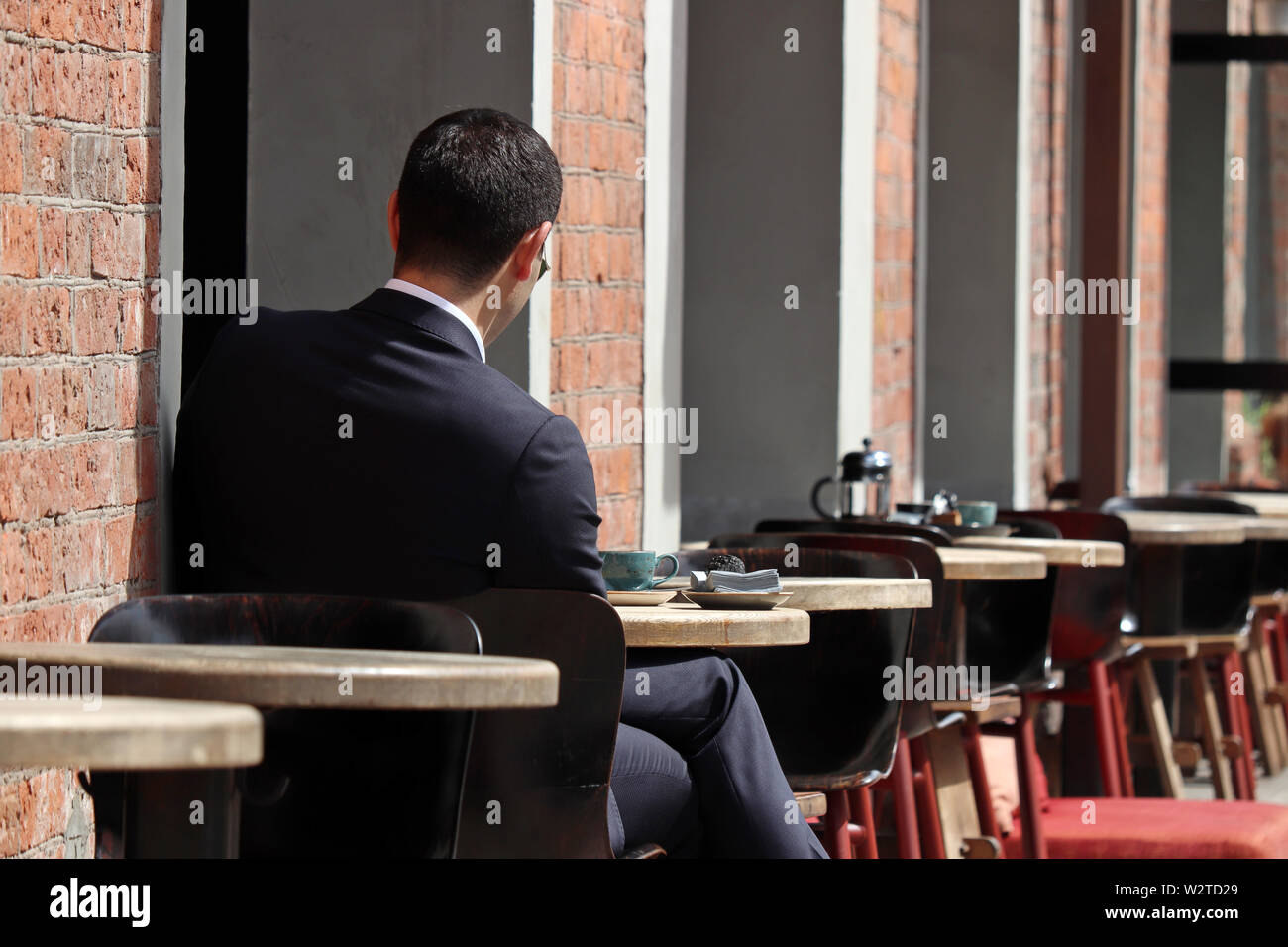 Stilvolle Mann in einen Anzug an einem Tisch sitzen in Street Cafe. Konzept der Mittagessen allein, Warten auf ein Datum oder eine geschäftliche Besprechung, Kaffeepause Stockfoto