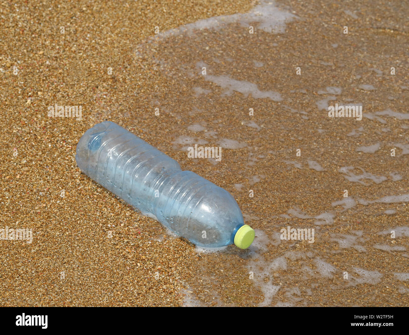 Kunststoff Flasche im Sand am Strand mit Wellen im Hintergrund, Konzept der Meeresverschmutzung durch Abfälle aus Kunststoffen Stockfoto