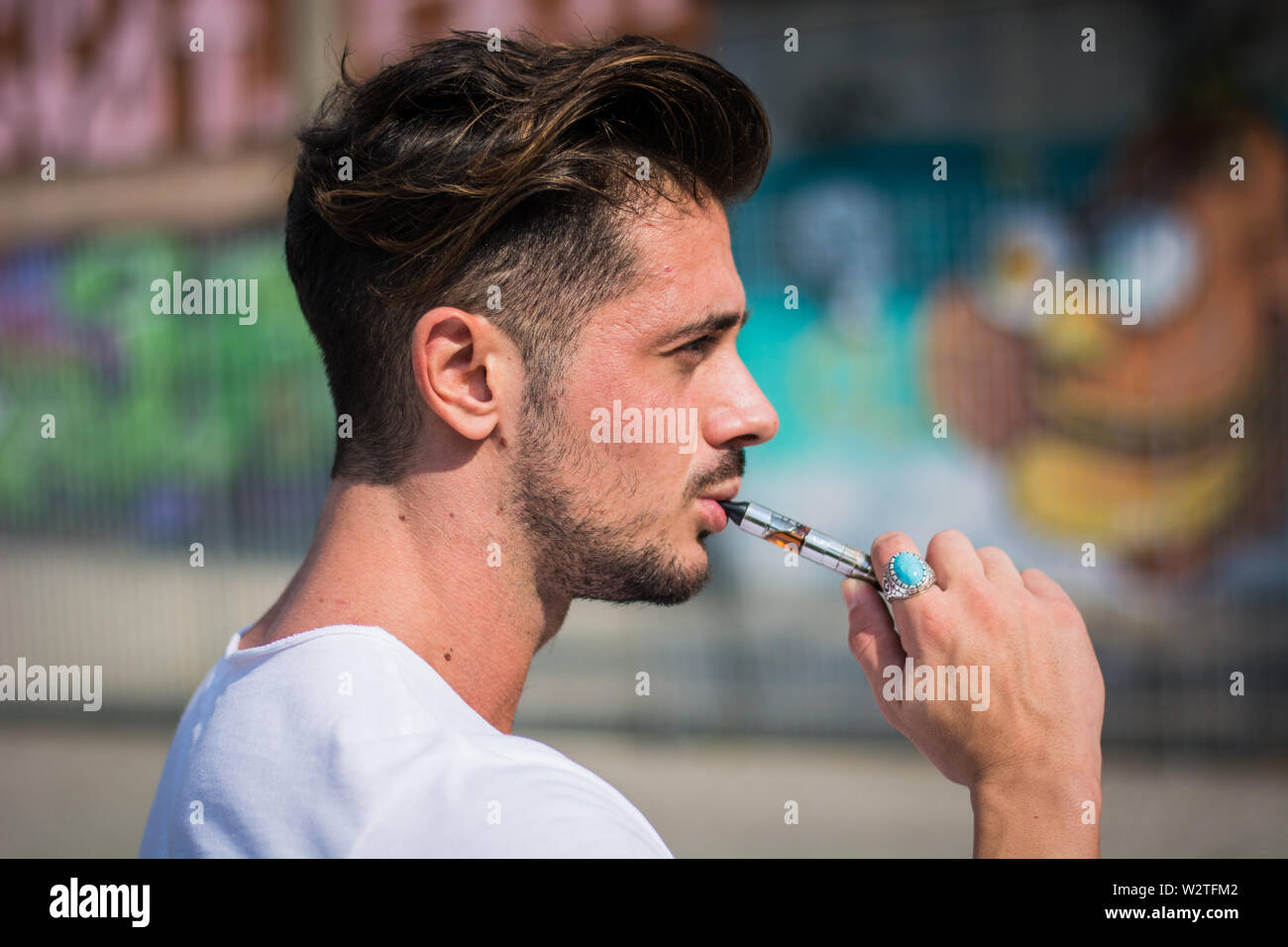 Schöner Mann, der eine E-Zigarette raucht und draußen dampft Stockfoto