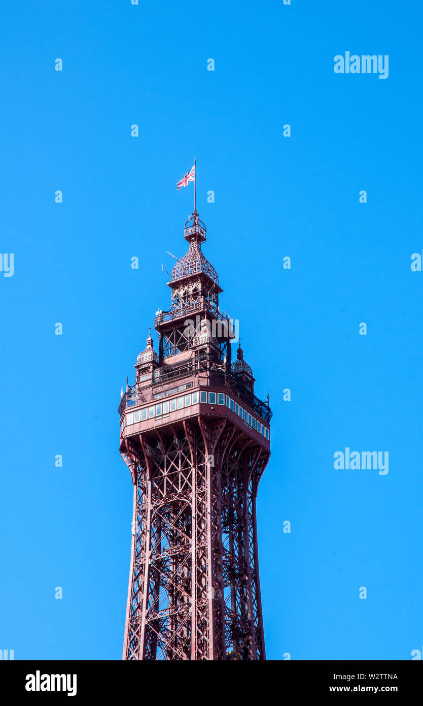 Die obere Hälfte der Blackpool Tower gegen einen strahlend blauen Himmel mit Aussichtsplattform Crows Nest und Flagge auf der Oberseite Stockfoto