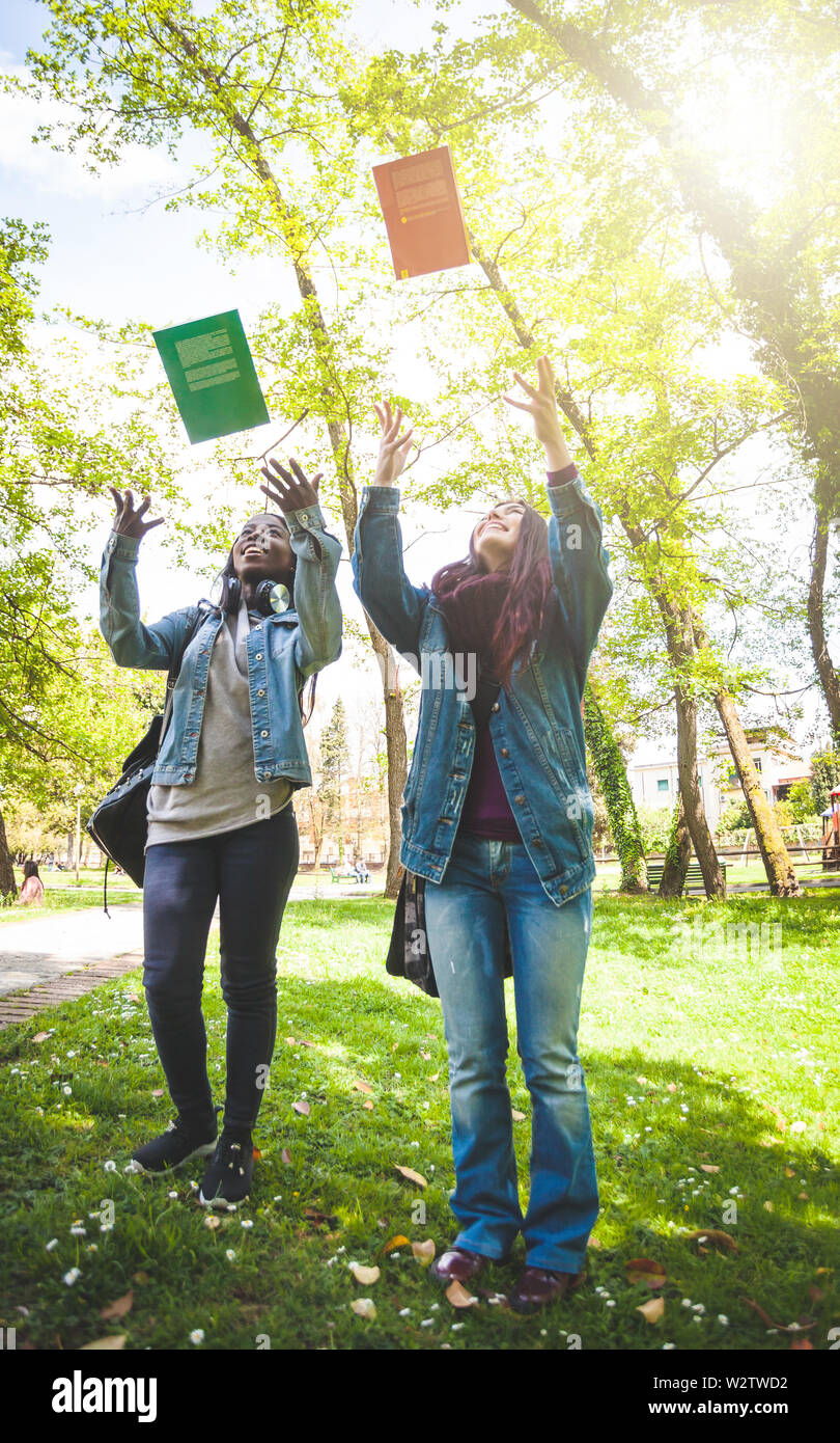 Zwei Studentinnen, einem kaukasischen und den anderen Afrikanischen, werfen Sie Bücher in die Luft. Ende des Studiums Konzept. Stockfoto