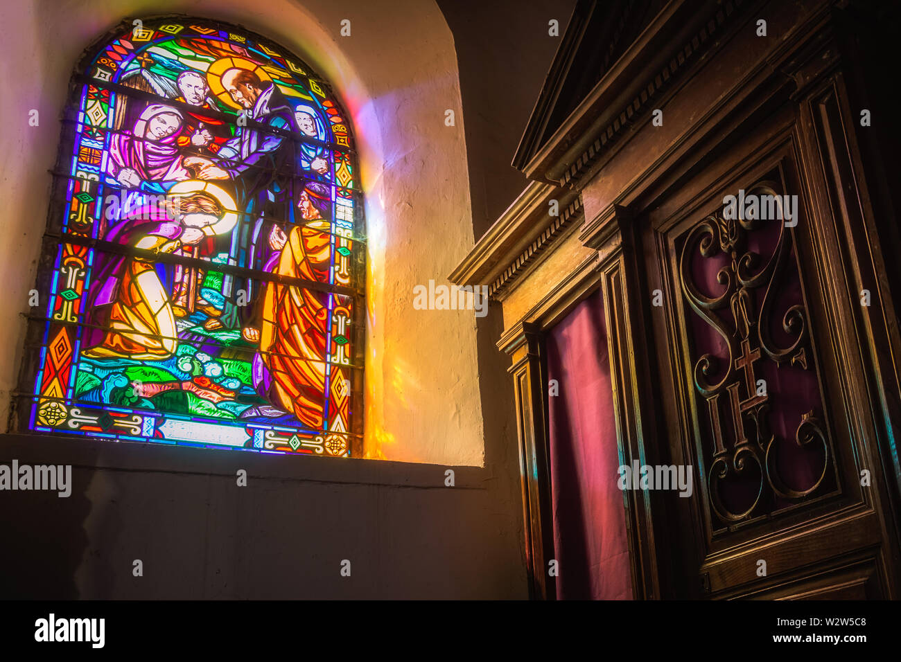 Holz- confessionnal mit violetten Vorhänge und religiösen Glasfenster in der Graal Kirche, oder Ste Onnene Kirche, Tréhorenteuc, Bretagne. Stockfoto