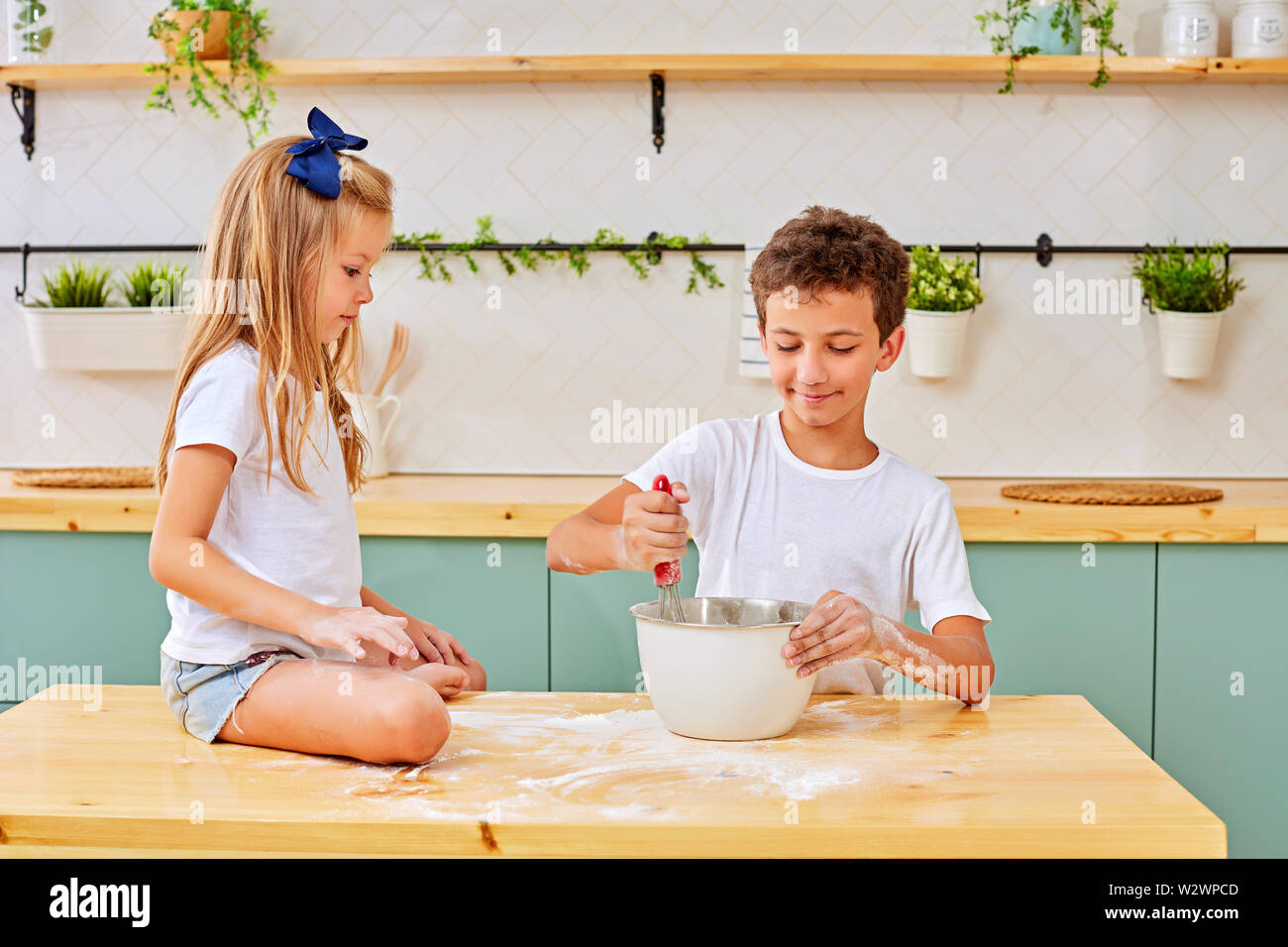 Kleine Jungen und Mädchen mischen frischen Teig für Gebäck in einer Schüssel beim Kochen in der Küche zu Hause zusammen Stockfoto