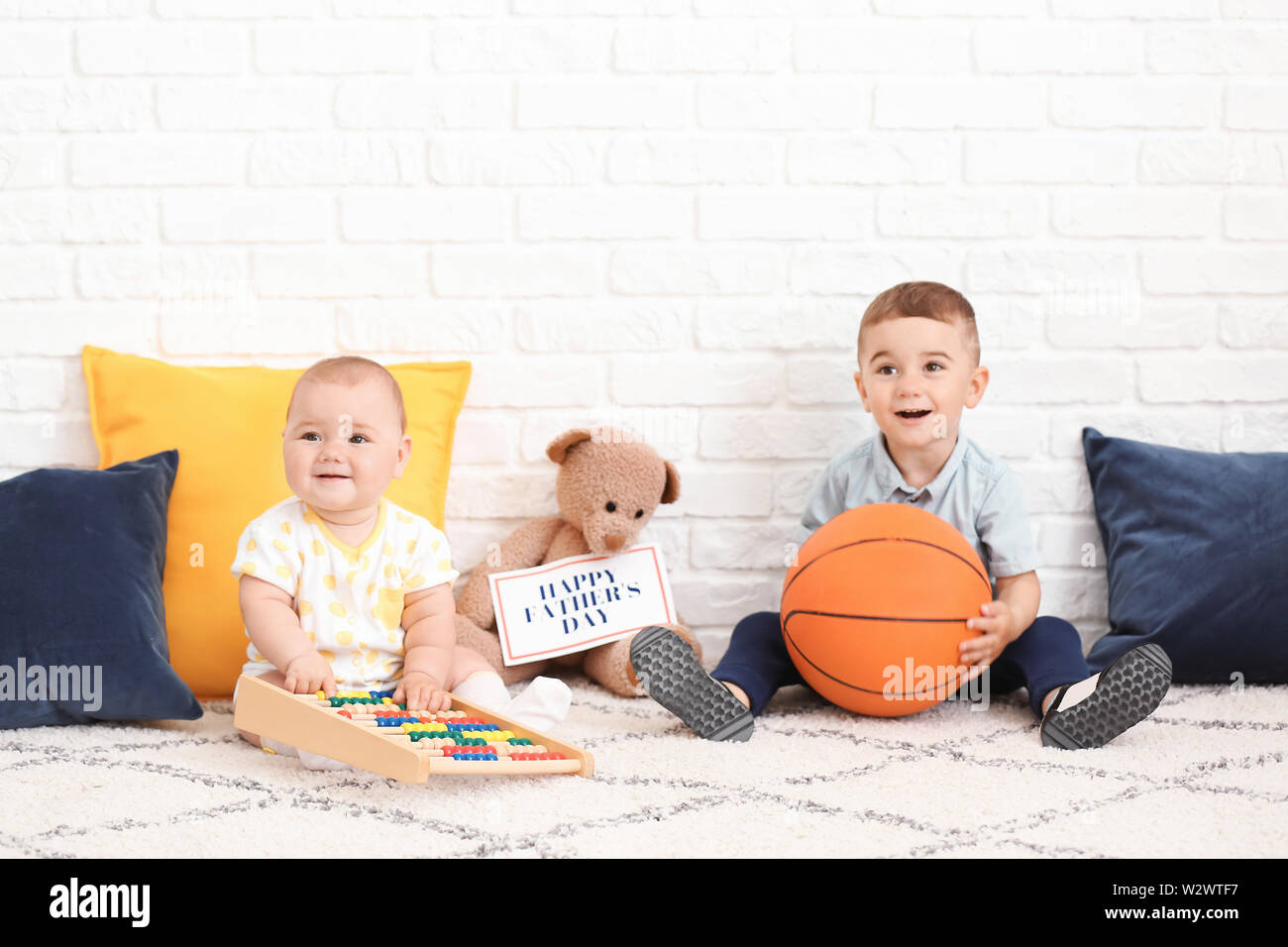 Süße kleine Kinder mit Spielzeug und Grußkarte für den Vatertag in der Nähe von White Brick Wall Stockfoto