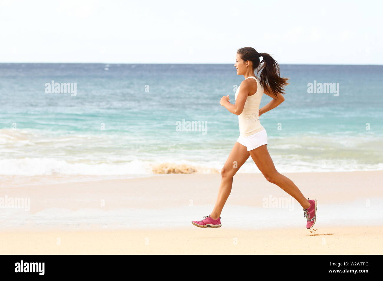Passen junge Frau läuft entlang der Kante des Surfen auf einem sonnigen tropischen Strand in ihrer Sportbekleidung mit ihren langen Haaren. Läuferin Trainieren mit Copyspace Stockfoto