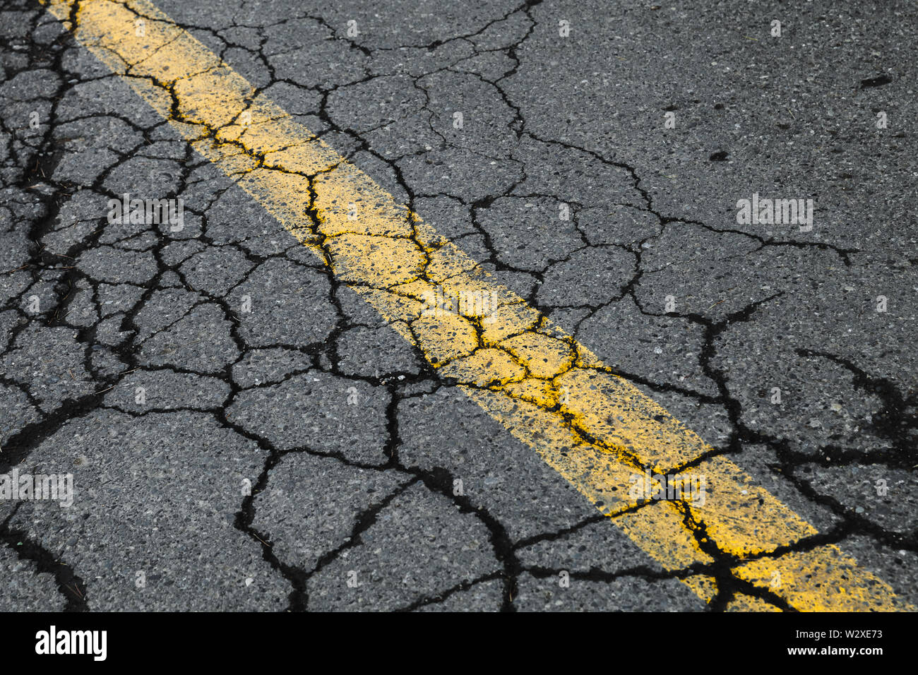 Risse im Asphalt mit gelben Trennlinie. Transport Hintergrund Textur Stockfoto