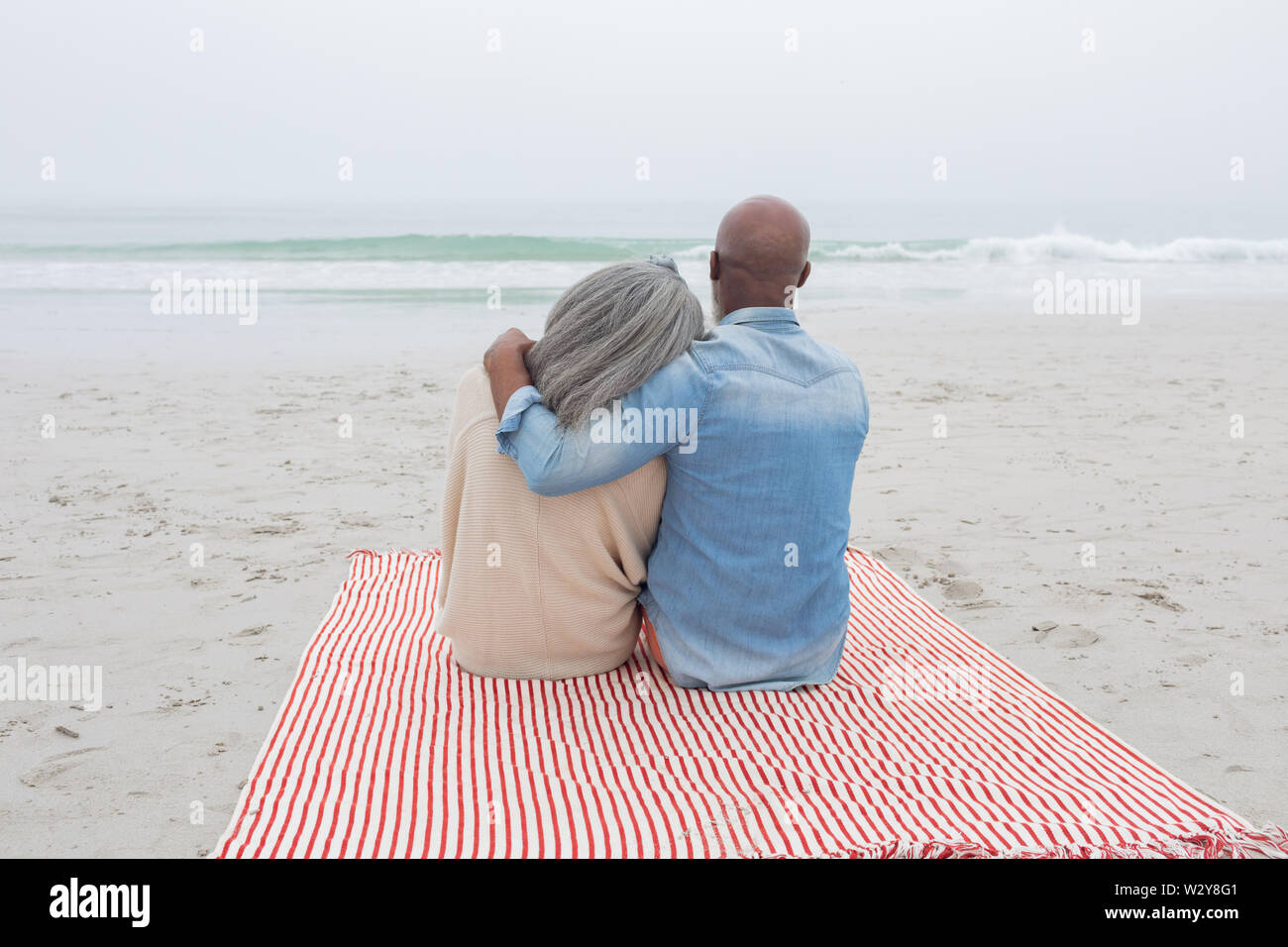 Paar sitzt auf rot-weiß gestreiften Picknickdecke am Strand Stockfoto