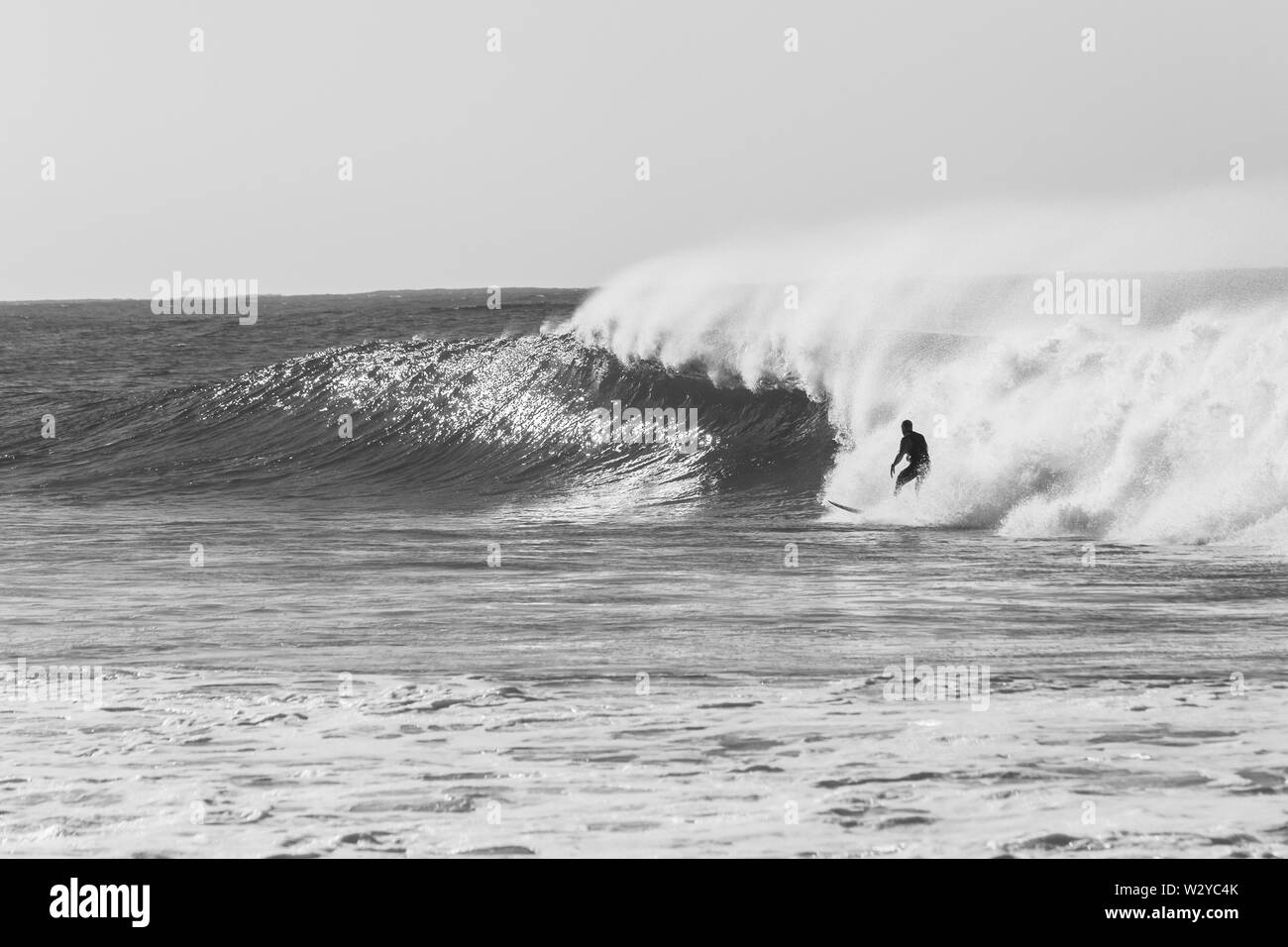 Surfer Surfen reiten links hinter dem Ocean Wave Absturz in Richtung Strand Küste in vintage Schwarz und Weiß. Stockfoto