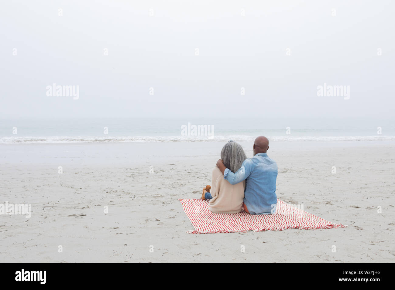 Paar sitzt auf rot-weiß gestreiften Picknickdecke am Strand Stockfoto
