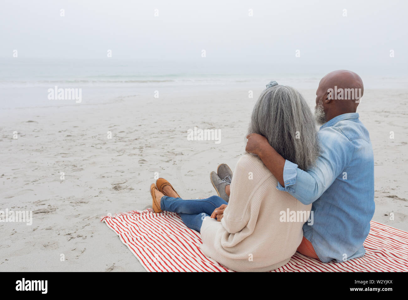 Paar sitzt auf rot-weiß gestreiften Picknickdecke am Strand Stockfoto