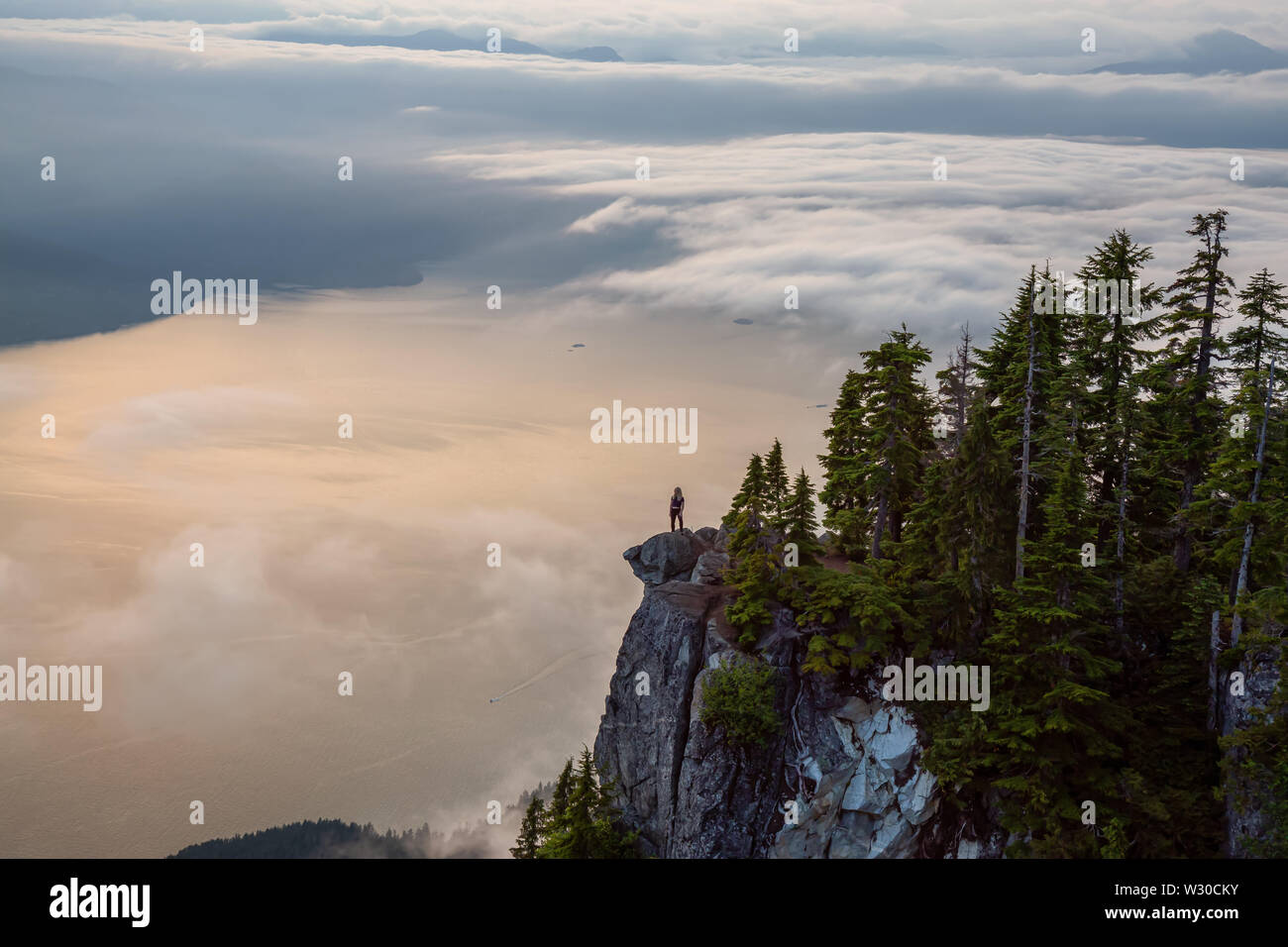 Weibliche Wanderer auf einem Berg in Wolken während einer lebhaften Sommer Sonnenuntergang abgedeckt. Auf dem St Mark's Summit, West Vancouver, British Columbia genommen Stockfoto