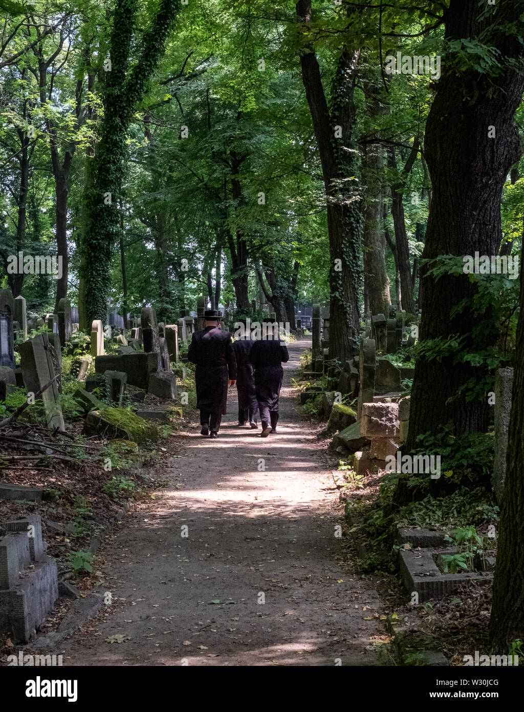 Jüdische Chasidic Männer in traditionellen lange schwarze Mäntel und Hüte sprechen Sie ein Gebet an einem alten Grabstein in der Neuen Jüdischen Friedhof in Kazimierz in Krakau, Polen Stockfoto