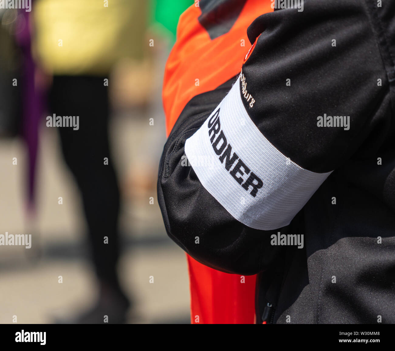 Arm einer Person mit einer schwarzen Jacke, auf dem eine weiße Binde mit der Inschrift 'Guard' und über den Namen der Stadt Wolfsburg sind ein Stockfoto