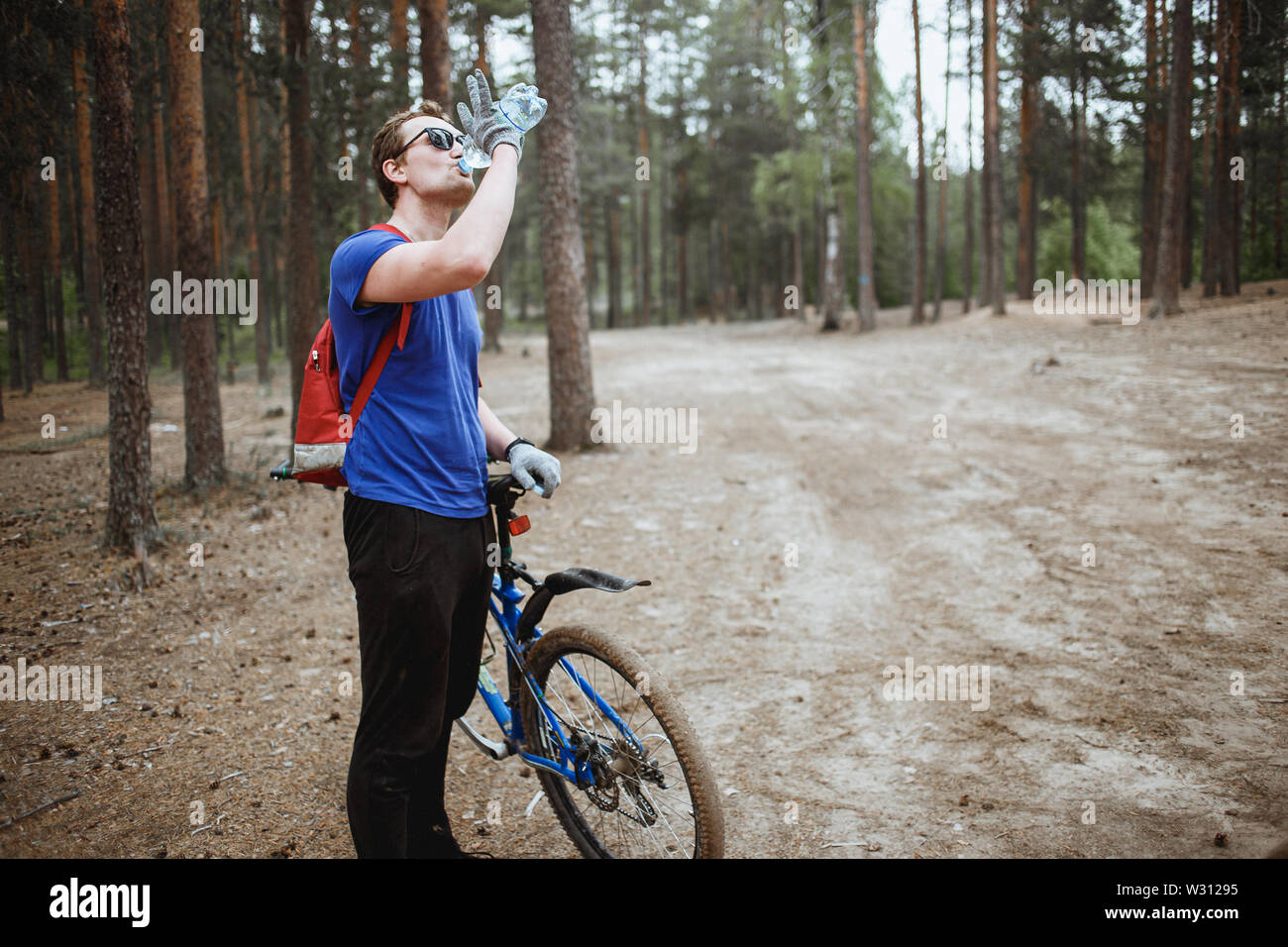 Hübscher junger Mann amateurl cyclistdrinking Wasser aus der Flasche, Fahrrad genießen in einem Pinienwald. Erholung der Sportler. Stockfoto