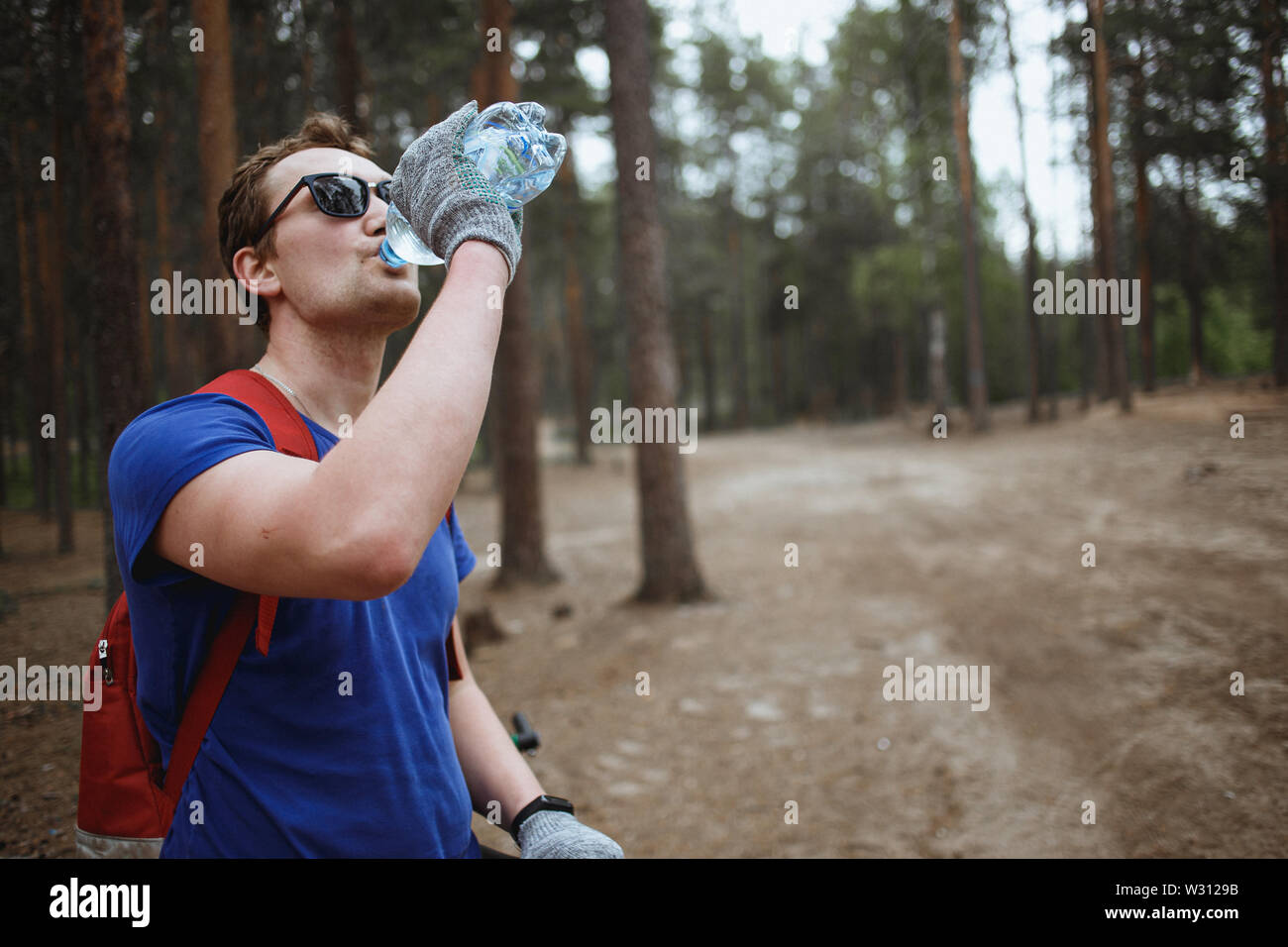 Hübscher junger Mann amateurl cyclistdrinking Wasser aus der Flasche, Fahrrad genießen in einem Pinienwald. Erholung der Sportler. Stockfoto