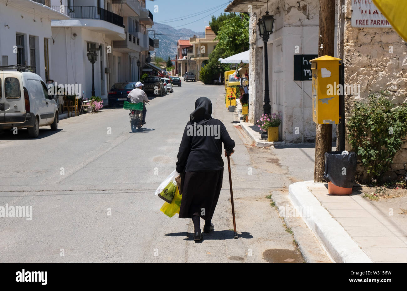 Ältere griechische Frau hinunter leere Straße im Dorf Agios Georgios, Lasithi Hochebene, Kreta Stockfoto