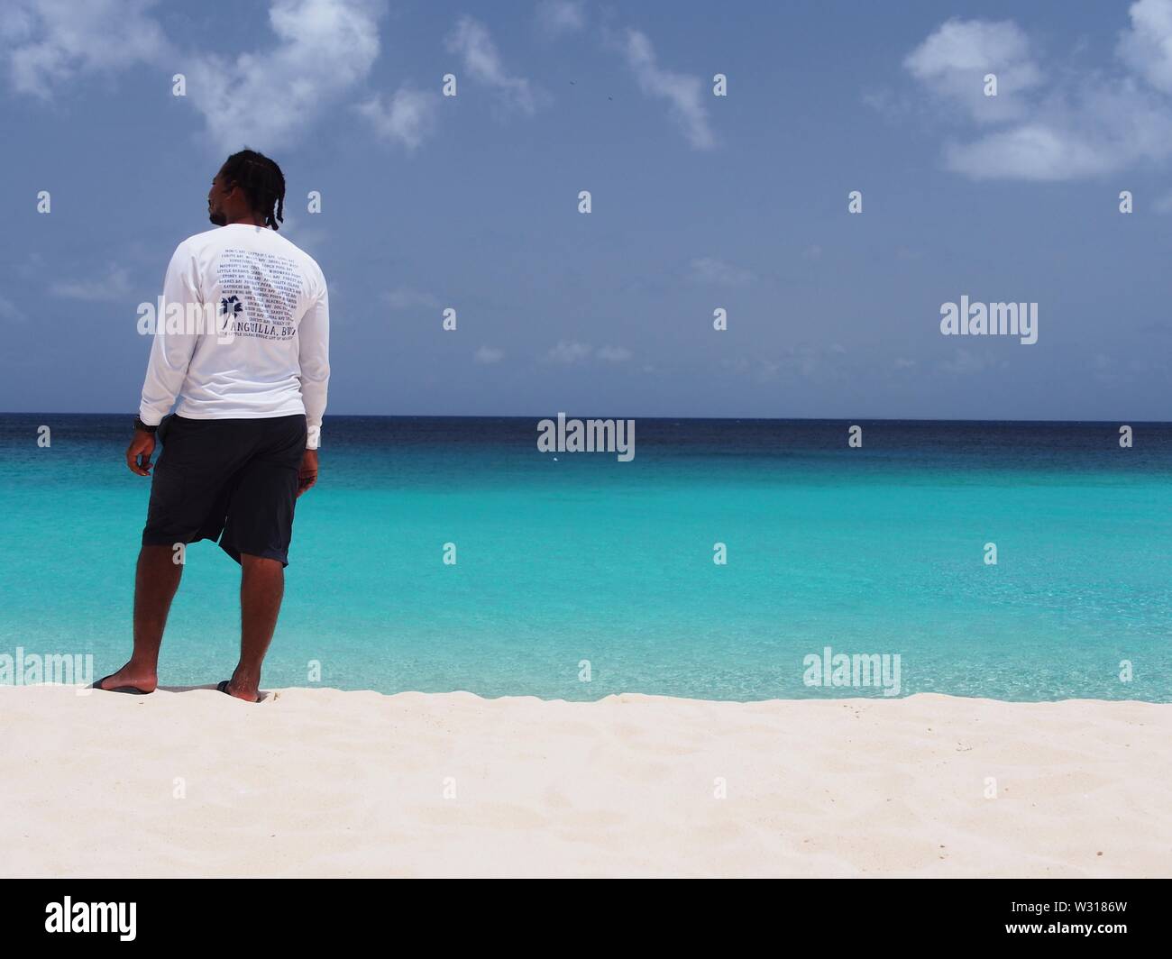 Anguillan Mann in einer weißen und schwarzen Shorts stehen auf dem Strand aufs Meer suchen, Meads Bay, Anguilla, BWI. Stockfoto