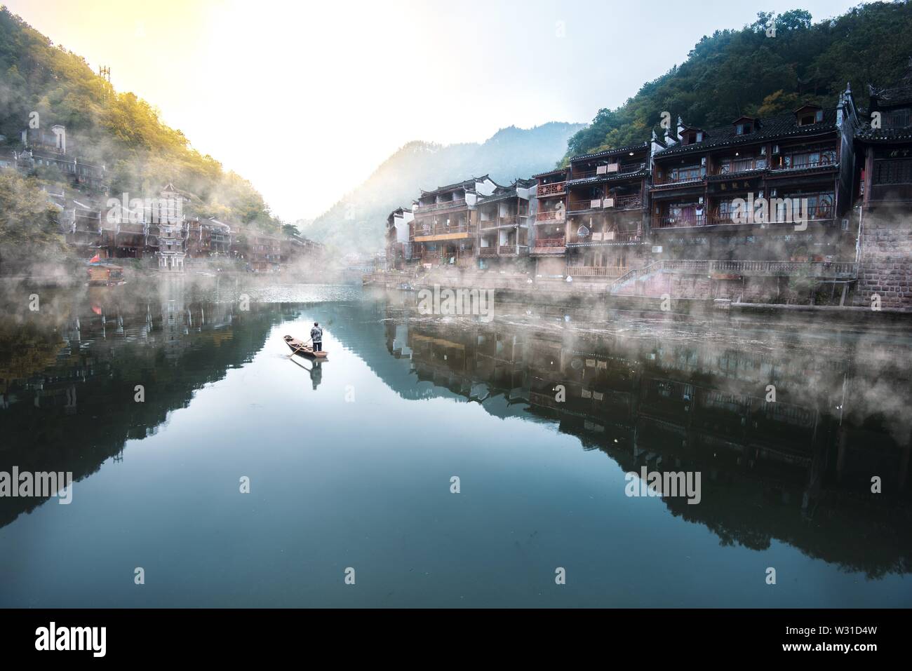 Ein lokaler Mann Reinigung der Fluss wie die Sonne in Fenghuang, China steigt. Stockfoto