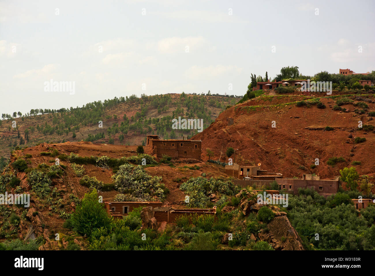 Ansicht der Berber Bergdörfer und Wohnungen im Atlasgebirge von Marokko Nordafrika, Grün robuste Bäume, Büsche und roten Schlamm Landschaft Stockfoto