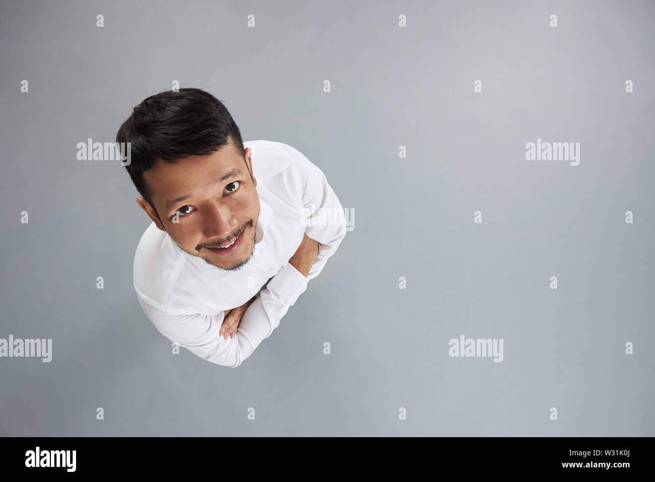 Jungen asiatischen Mann mit verschränkten Armen auf grauem Hintergrund über der oberen Ansicht isoliert Stockfoto