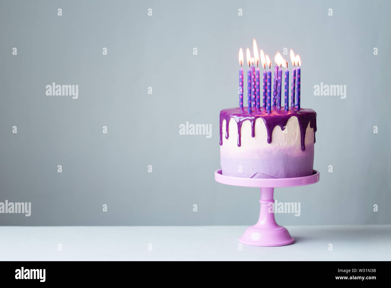Geburtstag Kuchen mit Tropf-stopp Vereisung und viel lila Kerzen vor grauem Hintergrund Stockfoto