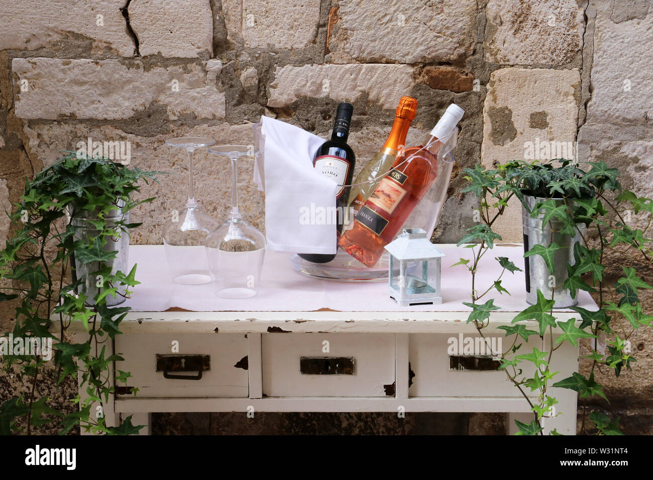 Weinflaschen und Gläser auf einem Beistelltisch im Freien Tageslicht gegen eine Steinmauer Stockfoto