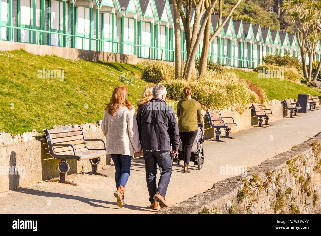 LANGLAND BAY, Gower, WALES - Februar 2019: Mann und Frau gehen Hand in Hand entlang der Promenade im Sonnenschein in Langland Bay auf der Gower Peninsula Stockfoto