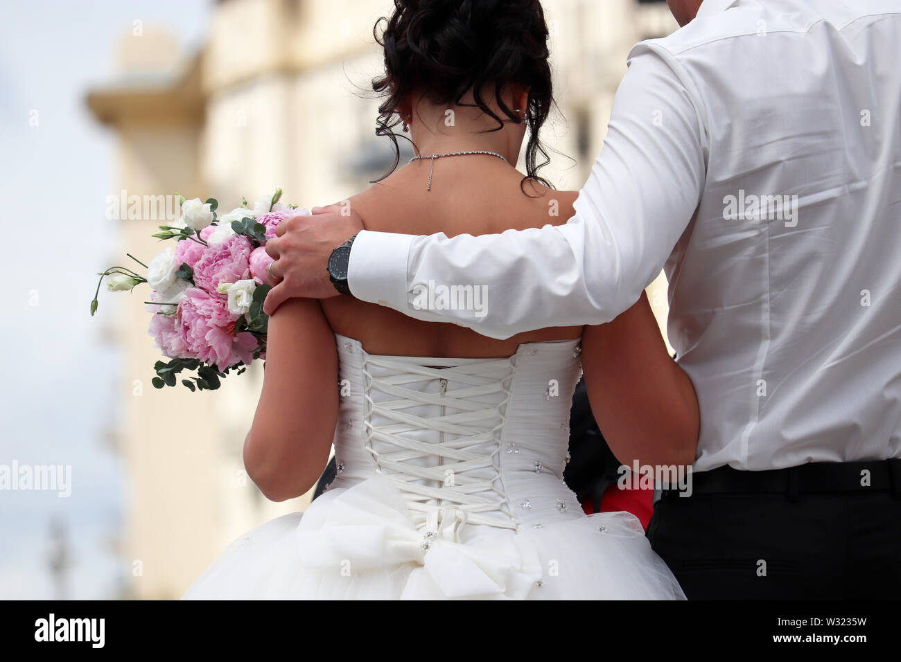 Frisch verheiratete Ehepaar, Bräutigam umfasst die Taille der Braut mit Blumenstrauß, Ansicht von hinten. Hochzeit in einer Stadt, das Konzept der neuen Familie Stockfoto