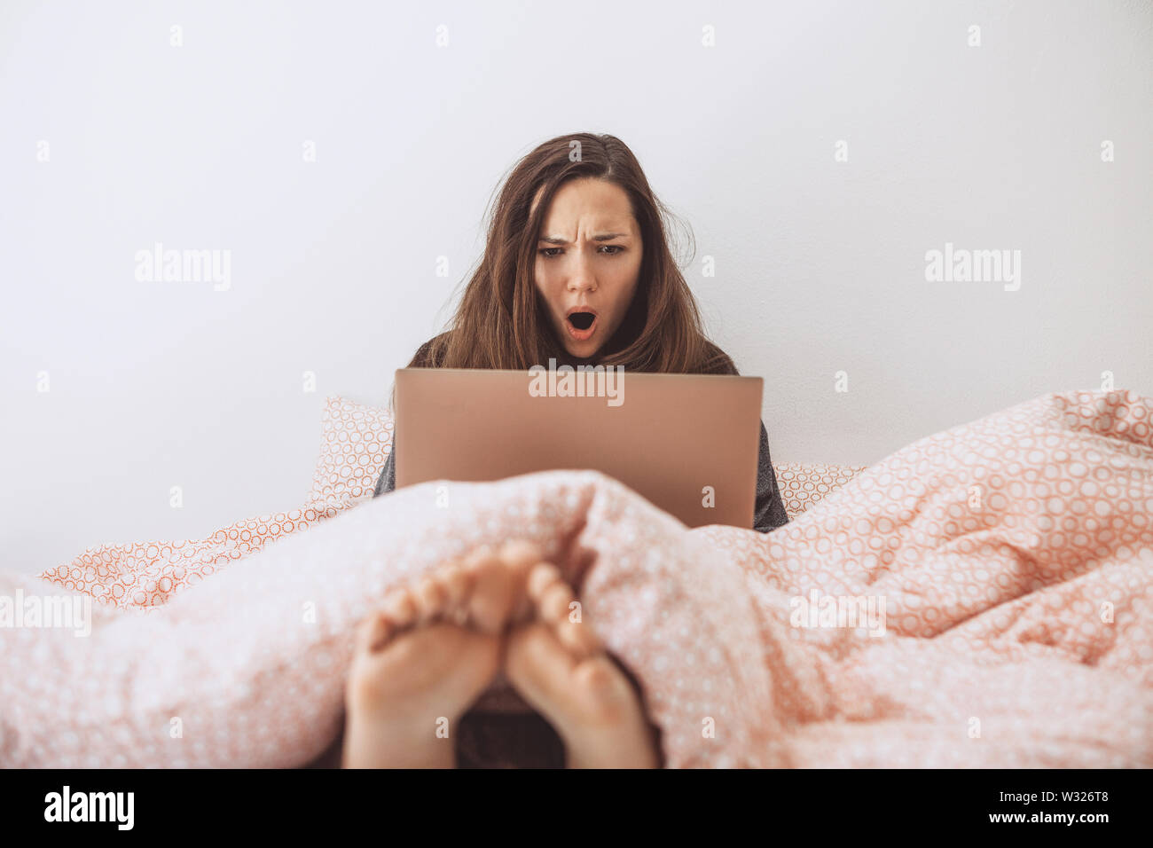 Das Mädchen mit dem Computer im Bett. Sie sah etwas und war überrascht und schockiert. Stockfoto