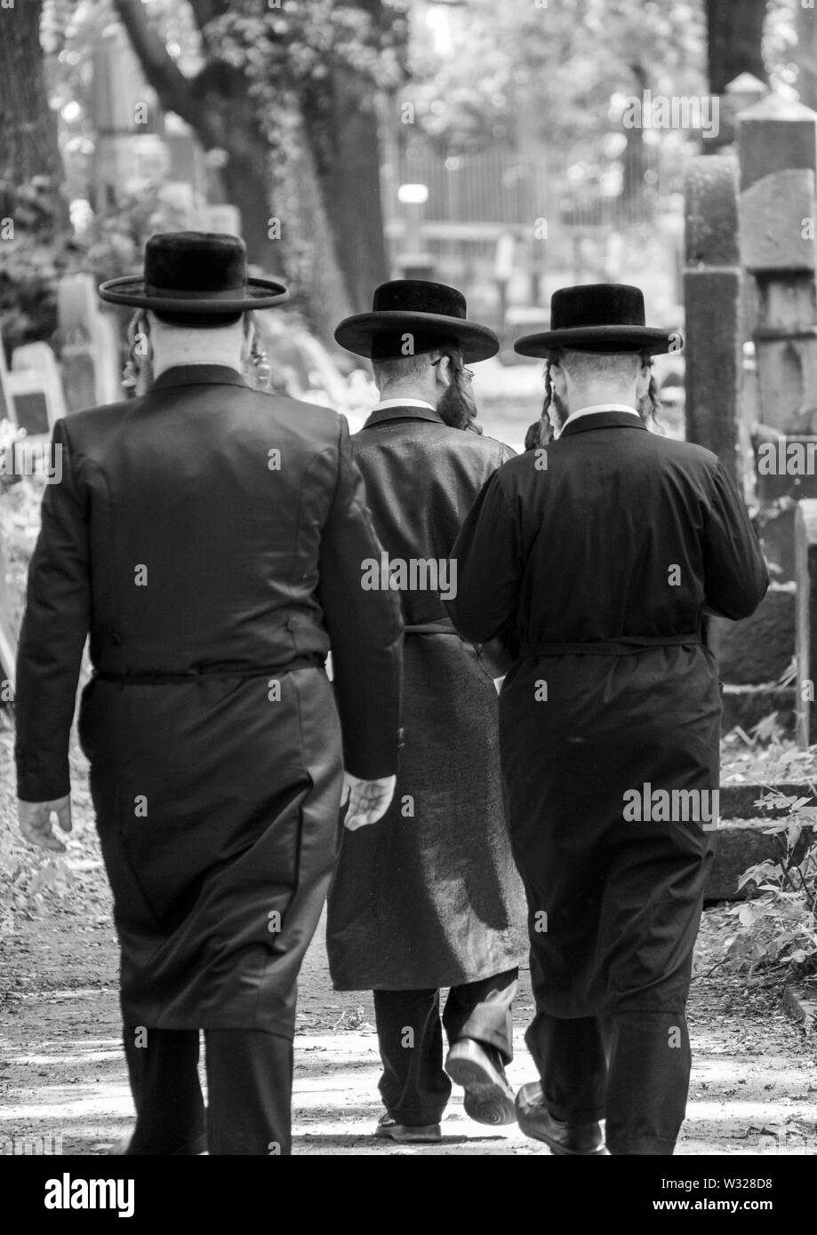Jüdische Chasidic Männer in traditionellen lange schwarze Mäntel und Hüte Spaziergang durch die alten Grabsteine in der Neuen Jüdischen Friedhof in Kazimierz in Krakau, Polen Stockfoto