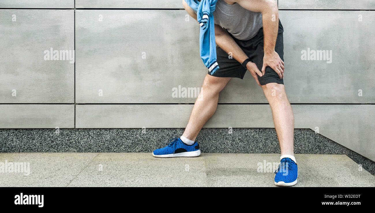 Knie schmerzen und Sport Verletzung. Junge Mann hält seine schmerzhaften Knie- und schlechte Gefühl. Sport und Gesundheit lifestyle Konzept. beschnitten und auf Grau w Stockfoto