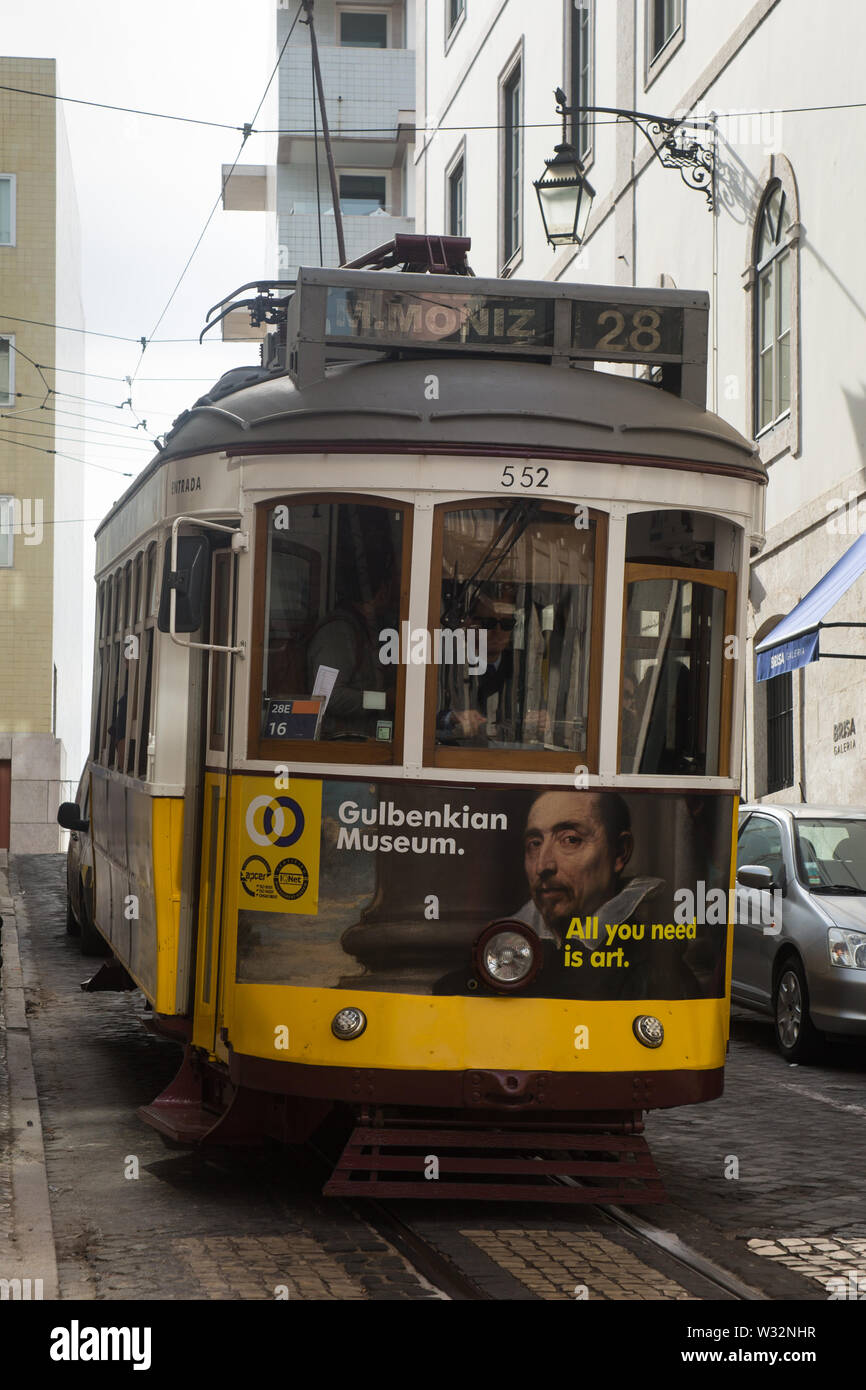 Gelbe und weiße vintage Straßenbahn auf die Straßenbahn 28 route (Wagen 552) Richtung Westen bergab auf engen, gepflasterten Straße der Stadt auf der Rua Vitor Cordon Lissabon, Portugal Stockfoto